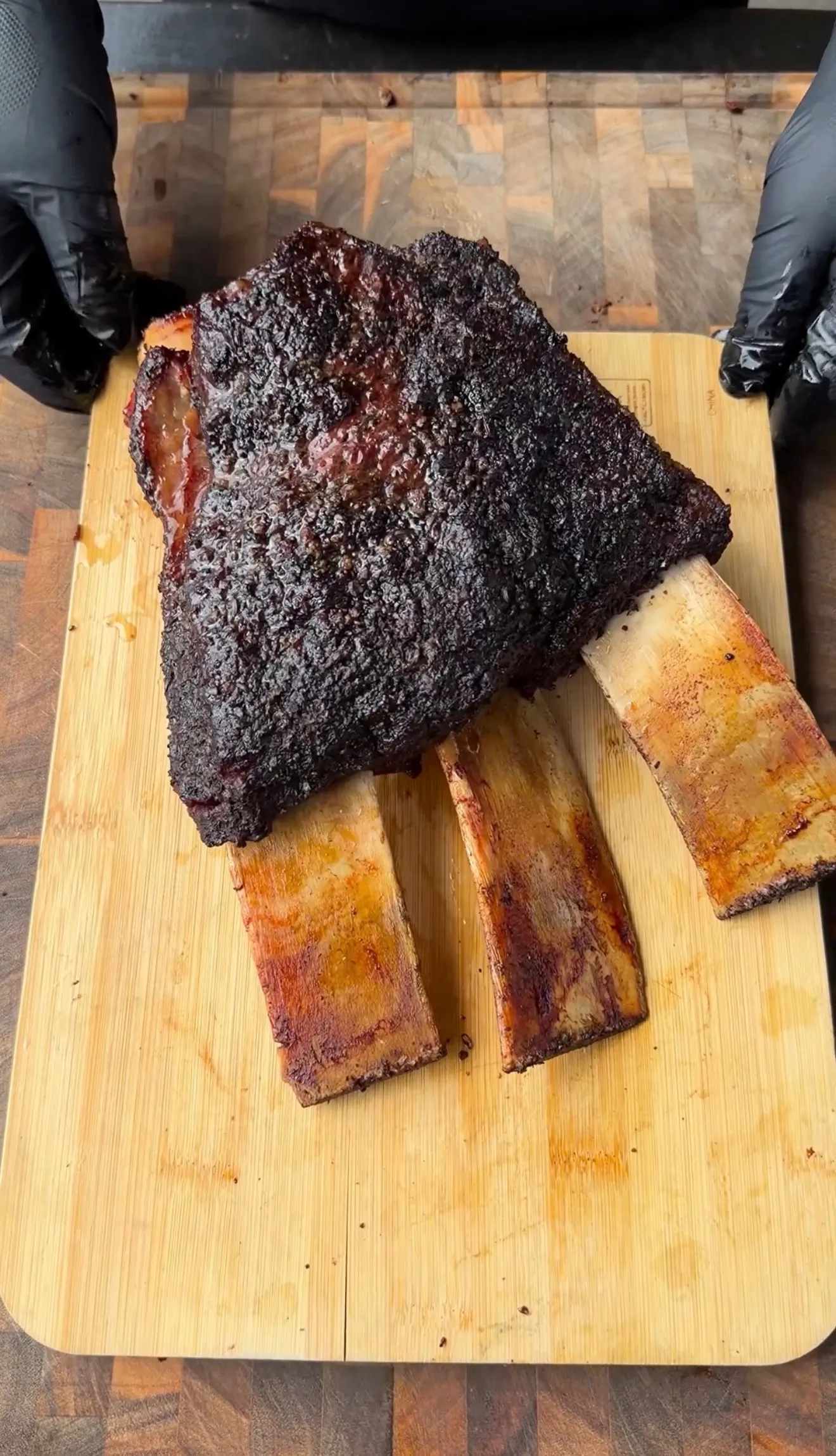 Massive hickory smoked beef plate ribs with dark bark crust resting on a wooden cutting board