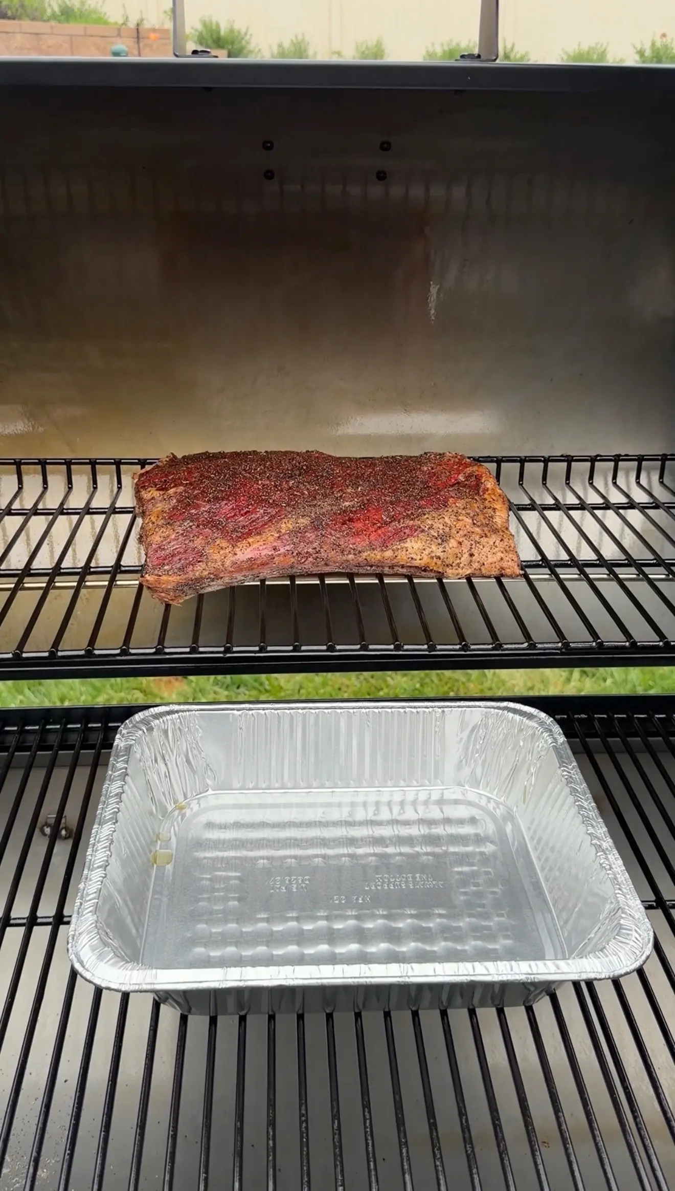 Seasoned beef plate ribs with pepper rub smoking on a pellet grill with a drip pan below