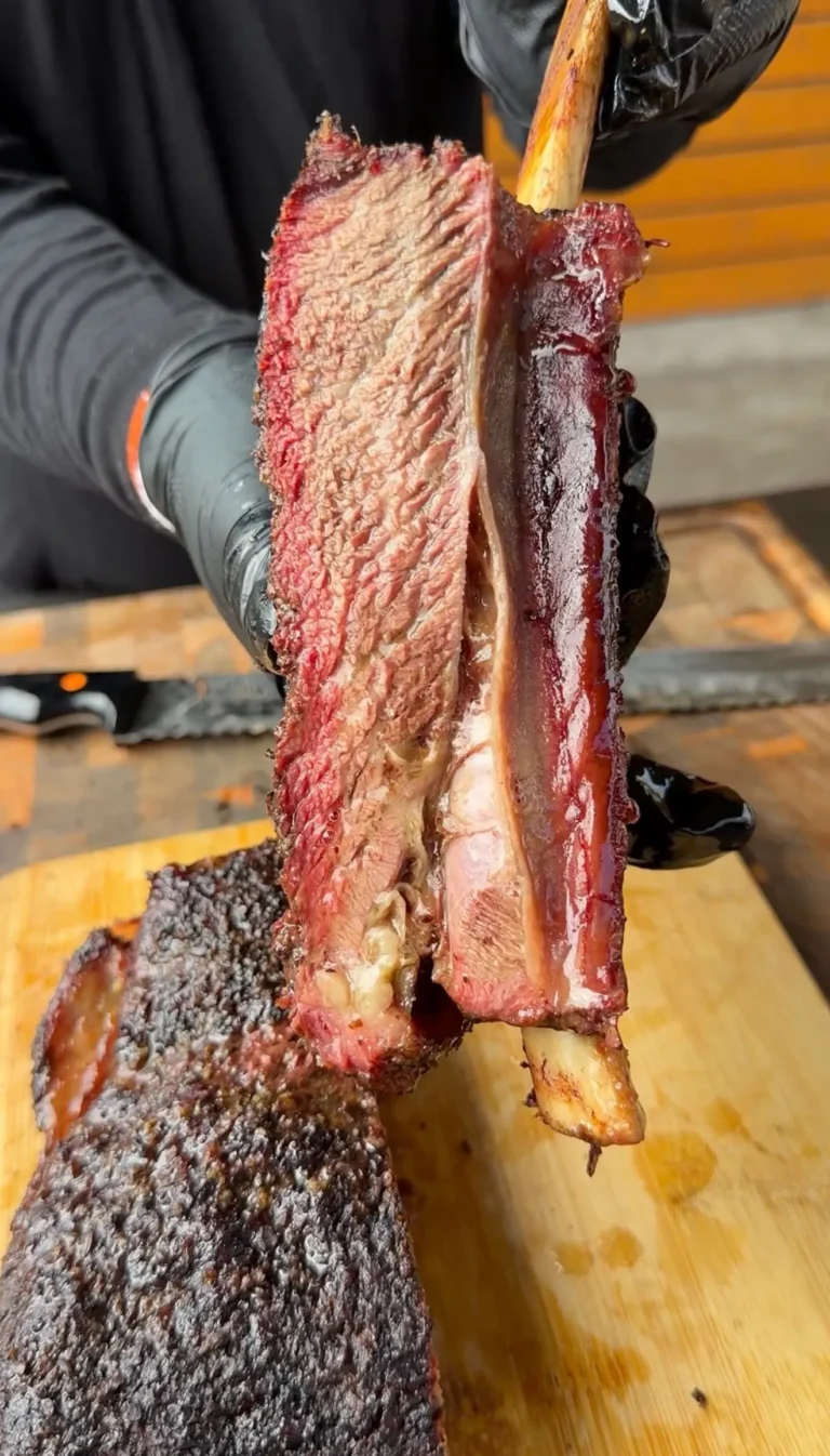 Hands pulling apart smoked beef plate ribs showing pink smoke ring and bark crust on a wooden cutting board