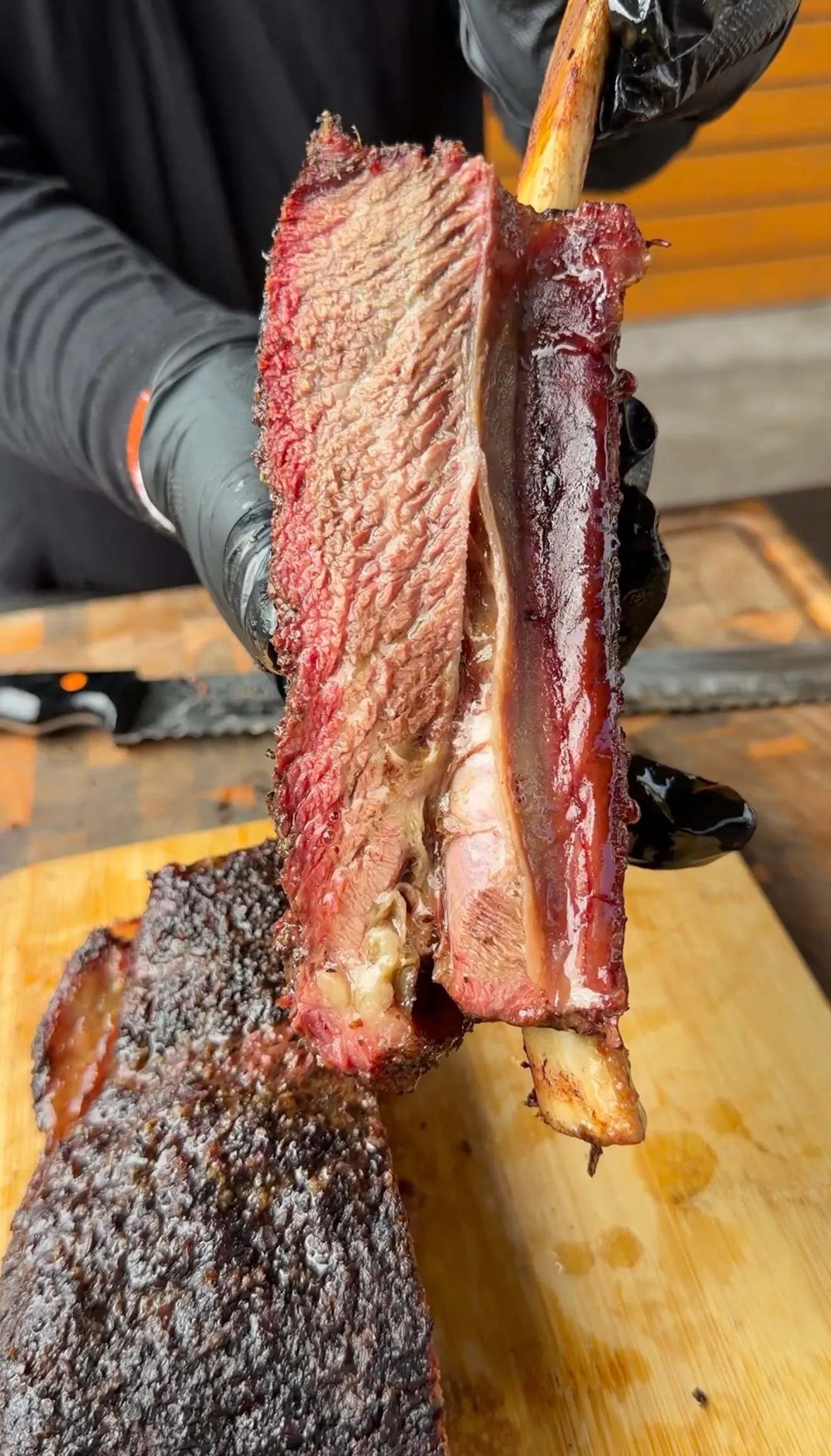 Hands pulling apart smoked beef plate ribs showing pink smoke ring and bark crust on a wooden cutting board