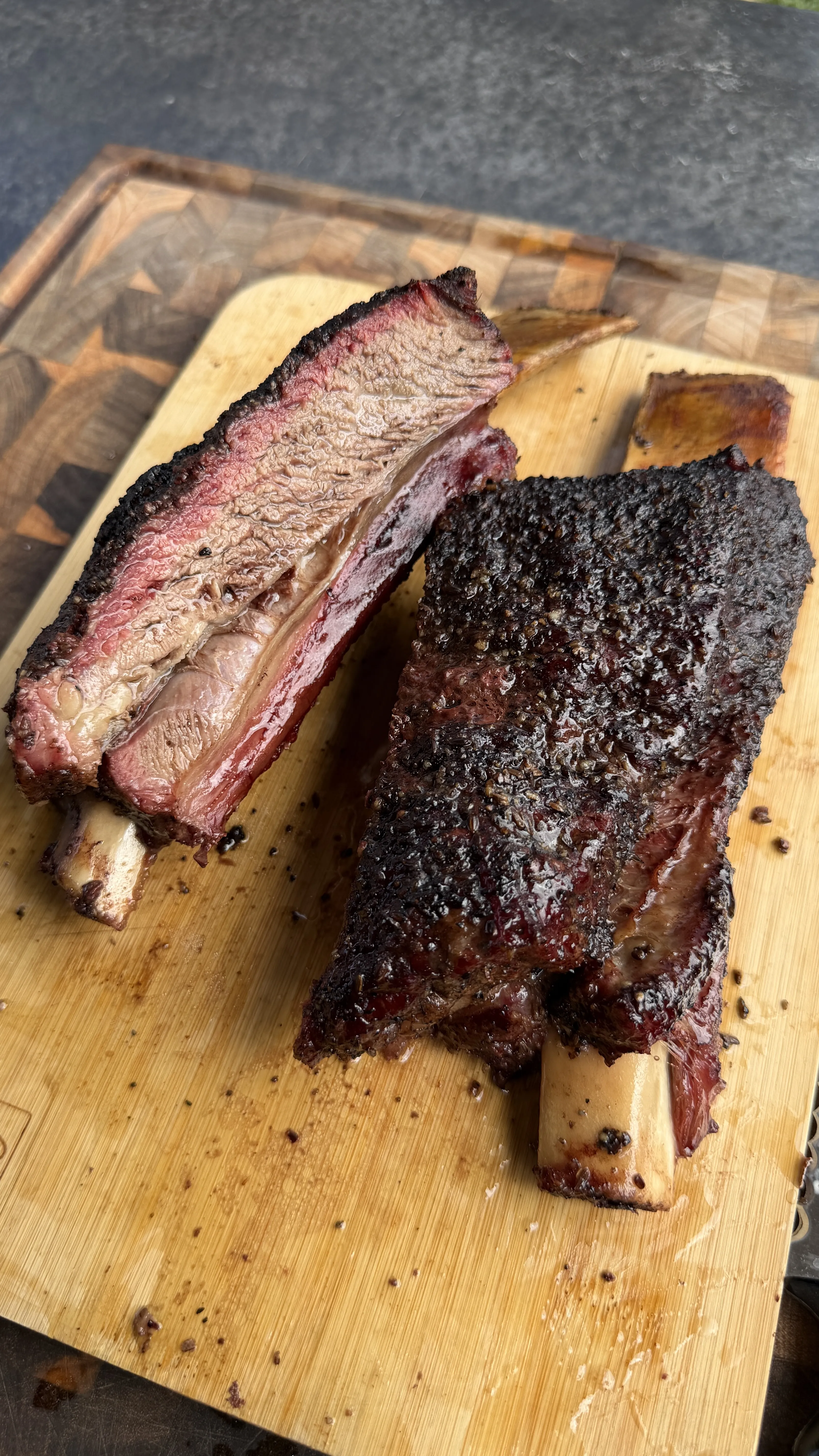 Hickory smoked beef plate ribs with dark bark crust, one sliced open showing pink smoke ring, on wooden cutting board