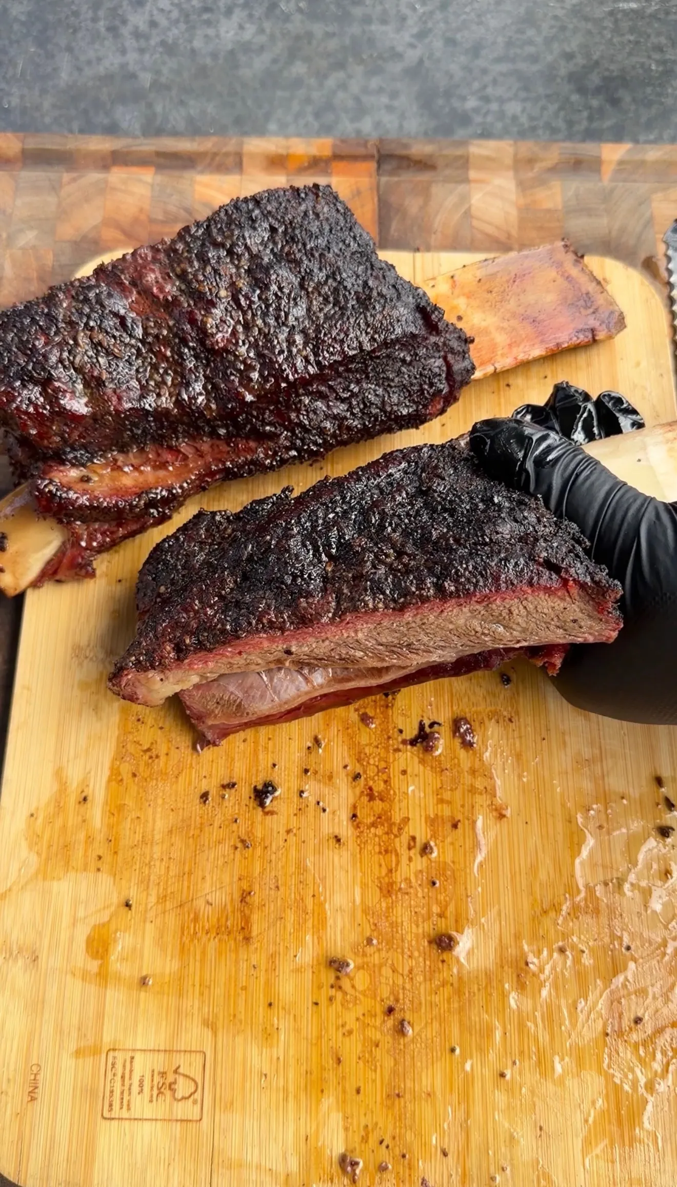 Hickory smoked beef plate ribs with dark bark crust, sliced open to reveal pink smoke ring on wooden cutting board