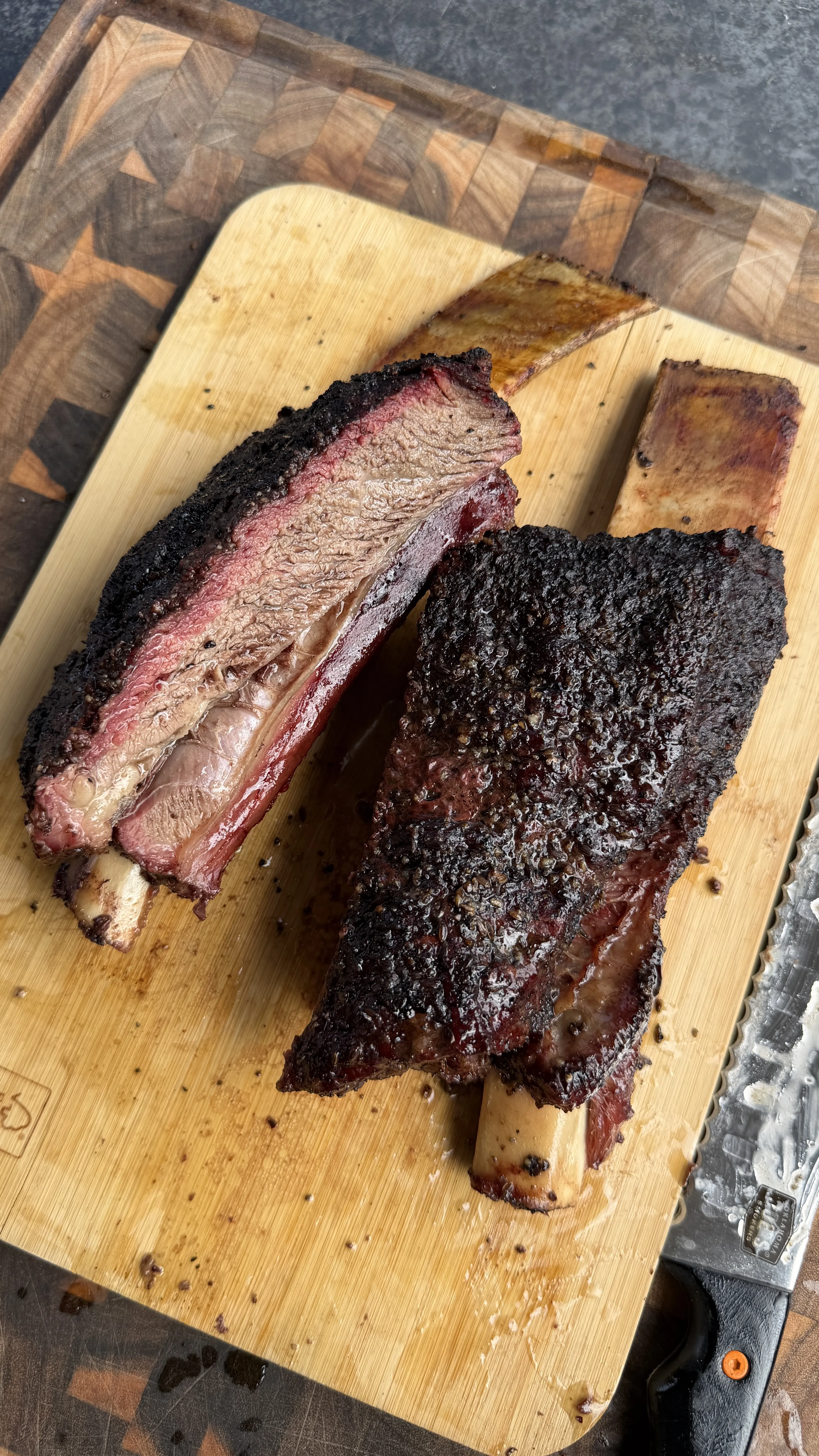 Hickory smoked beef plate ribs with dark bark crust, sliced open to reveal pink smoke ring on wooden cutting board