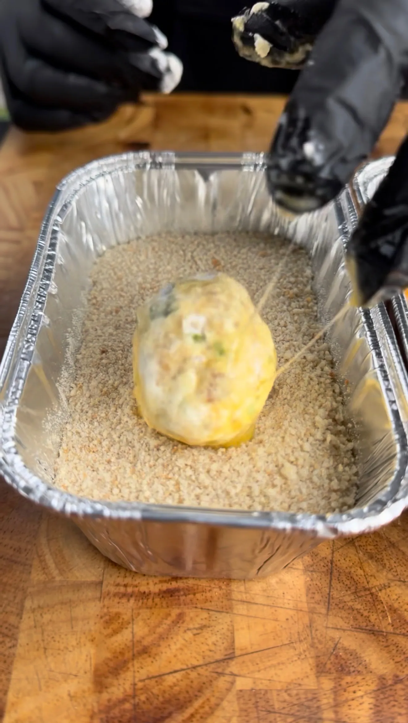 Egg-washed jalapeño popper bite being coated in seasoned breadcrumbs in an aluminum pan