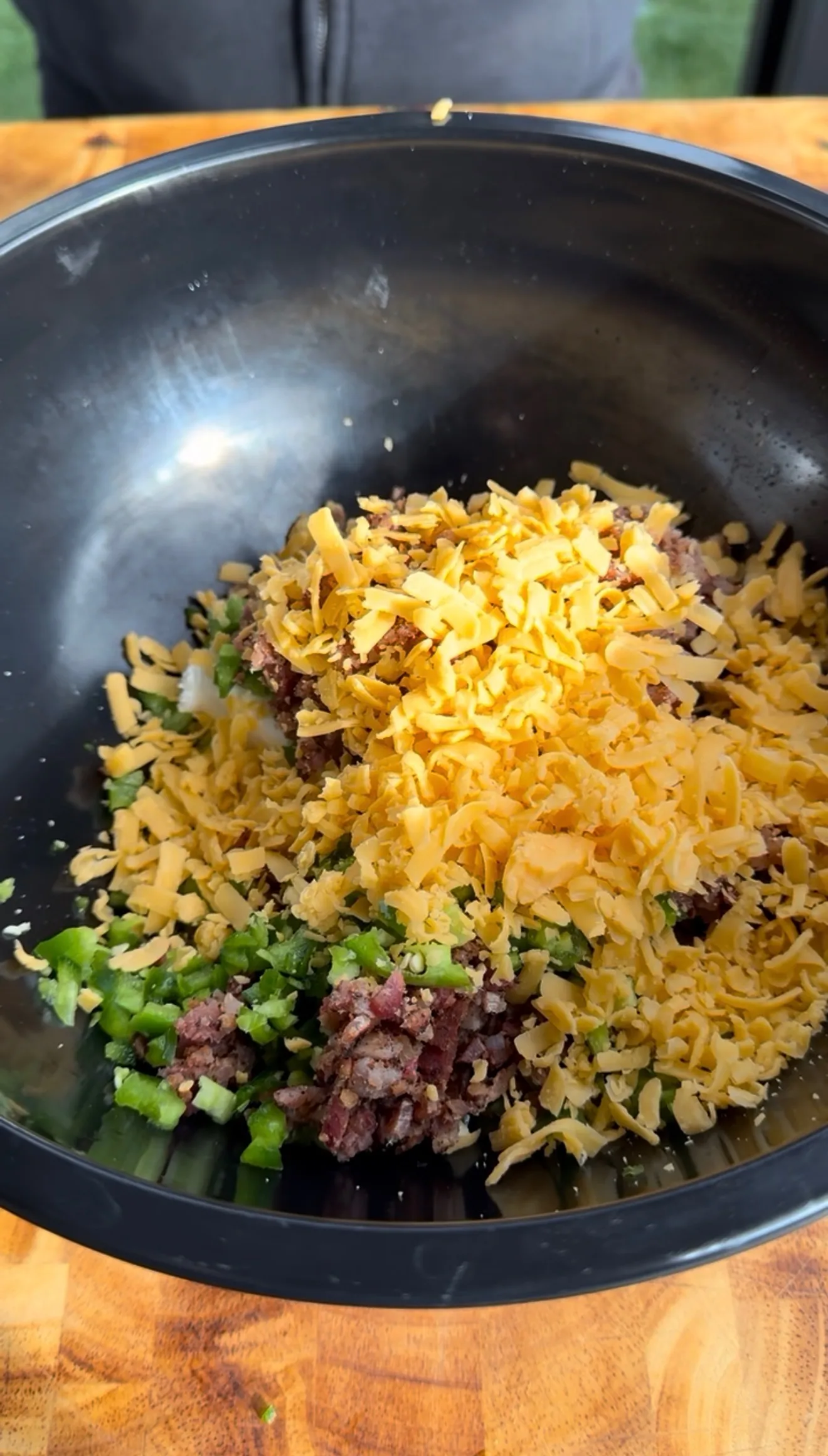 Black mixing bowl with shredded cheddar cheese, diced jalapeños, and bacon filling for deep fried jalapeño popper bites