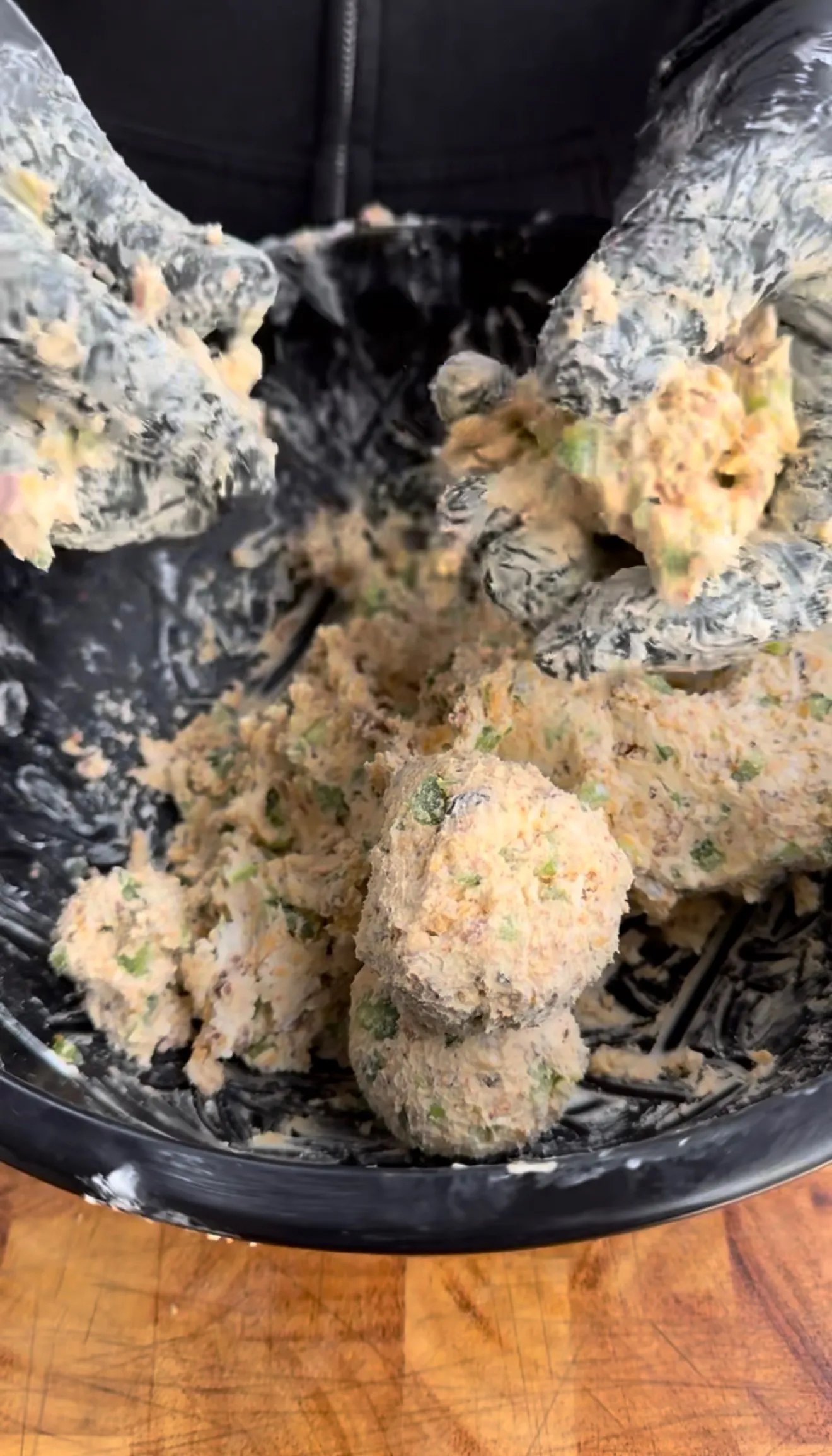 Hands in black gloves mixing and forming jalapeño popper bite balls in a large black bowl