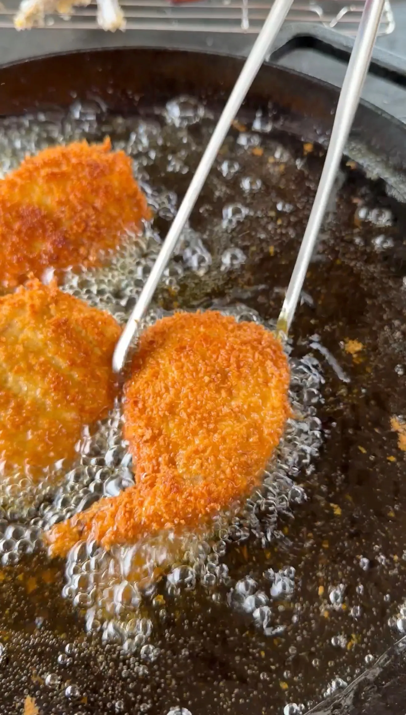 Breaded jalapeño popper stuffed shrimp deep frying in bubbling hot oil with metal tongs