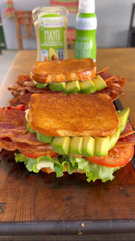 Tall avocado BLT sandwich with grilled sourdough bread, crispy bacon, fresh lettuce and tomato on wooden board