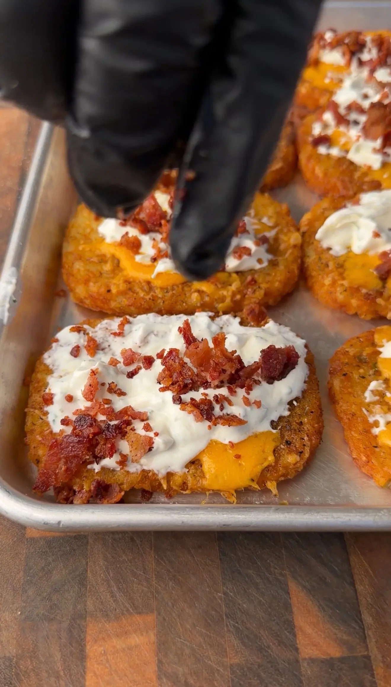 Golden crispy hash browns topped with melted cheese, sour cream, and crumbled bacon on a baking sheet