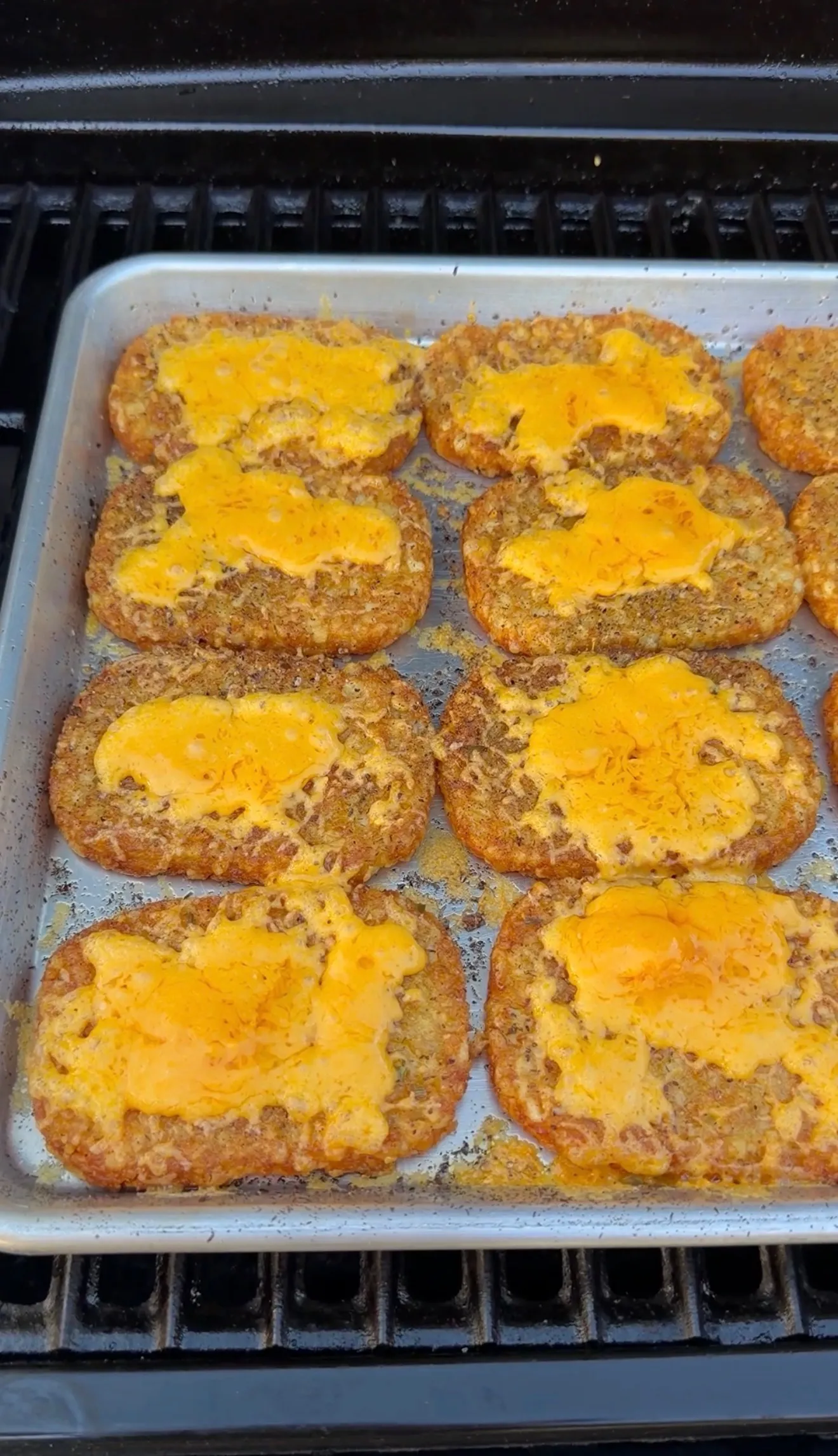 Golden crispy hash brown patties topped with melted orange cheese on a baking sheet in the oven