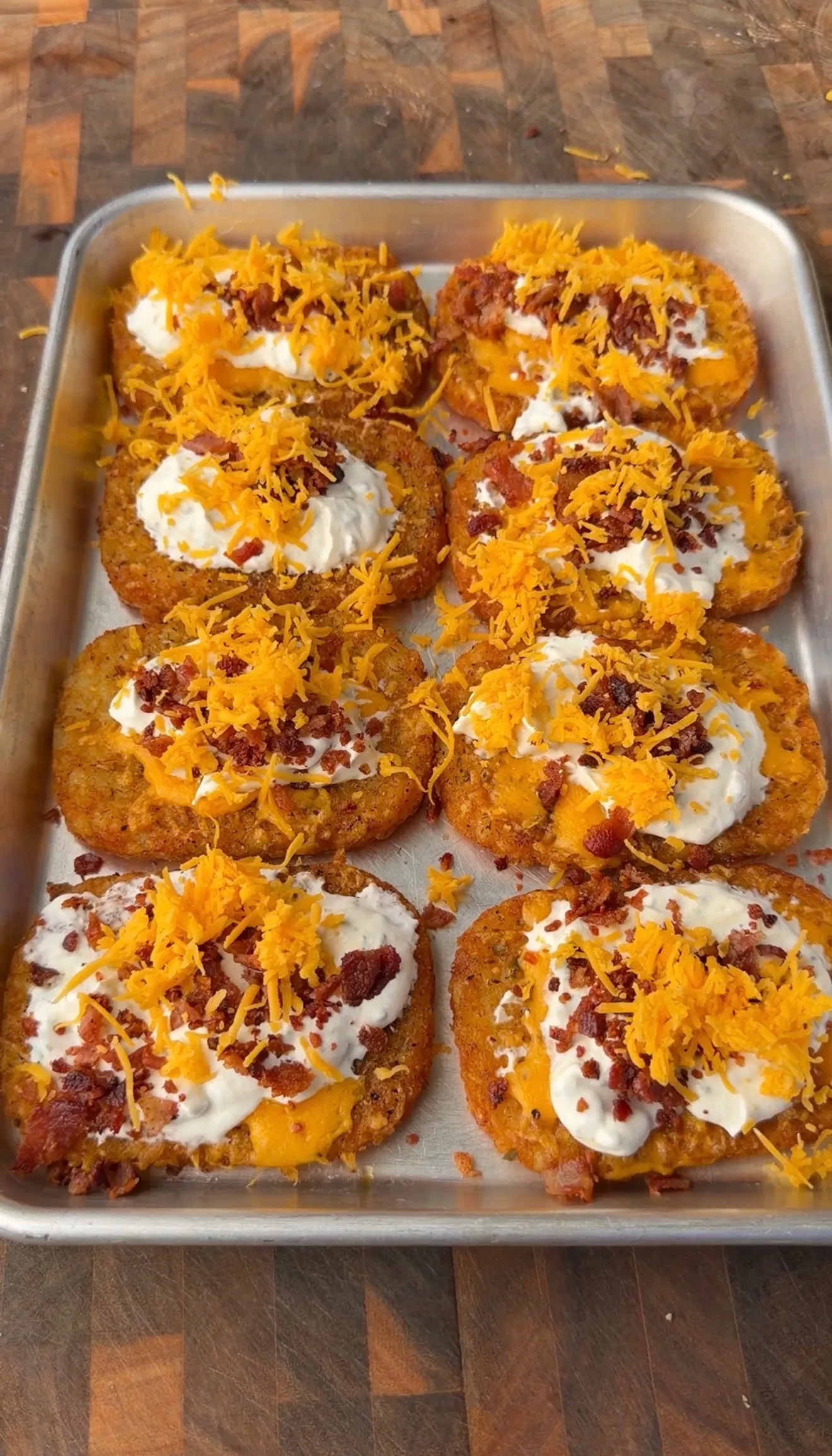 Loaded crispy hash browns topped with melted cheese, bacon bits, sour cream and chipotle aioli on baking sheet