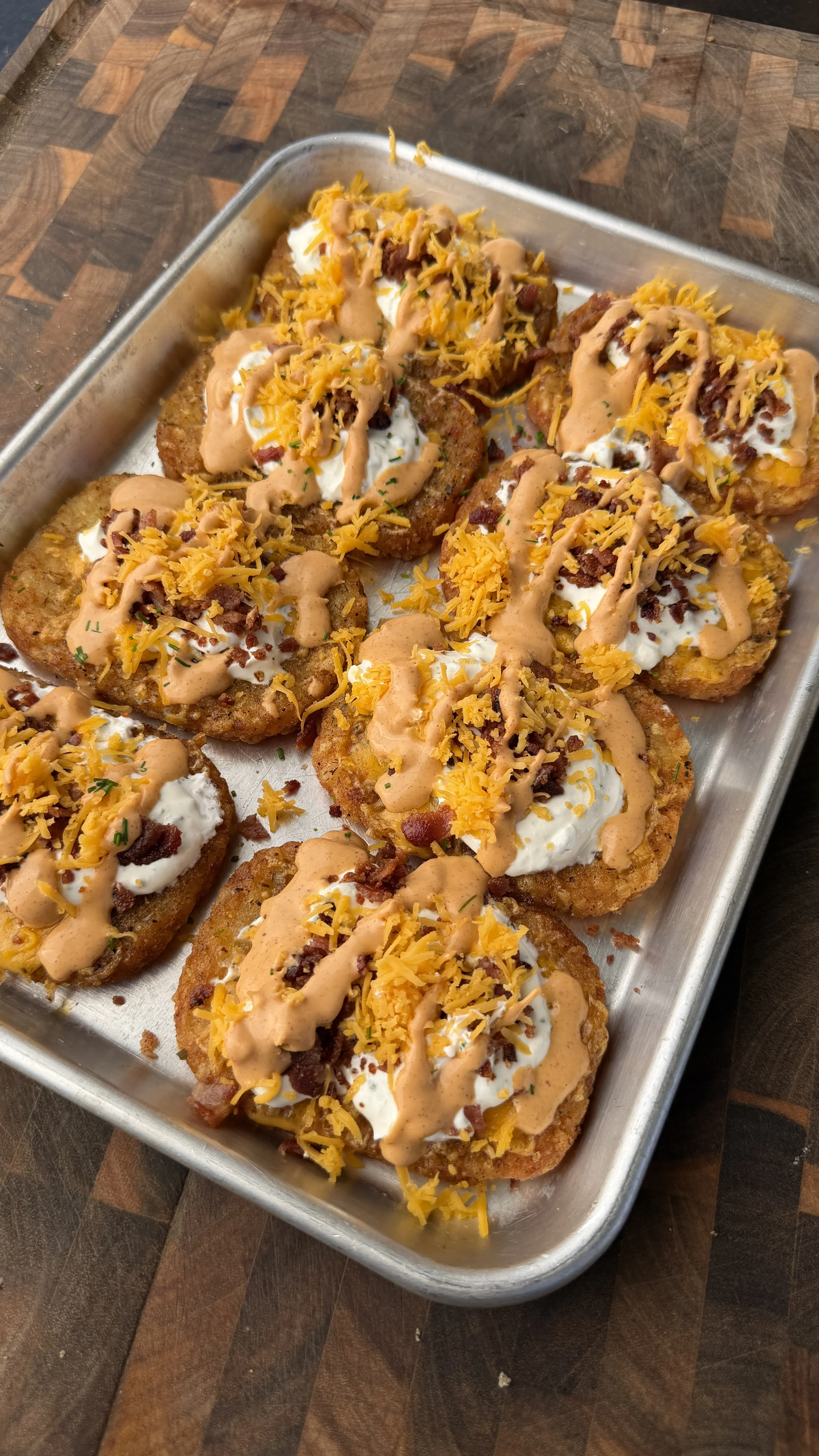Loaded crispy hash browns topped with melted cheese, bacon bits, sour cream and sauce on a metal baking sheet