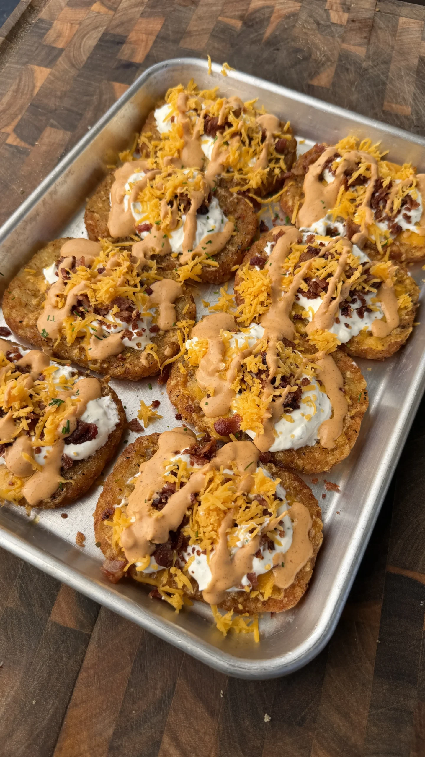 Loaded crispy hash browns topped with sour cream, cheese, bacon bits and sauce on a baking tray