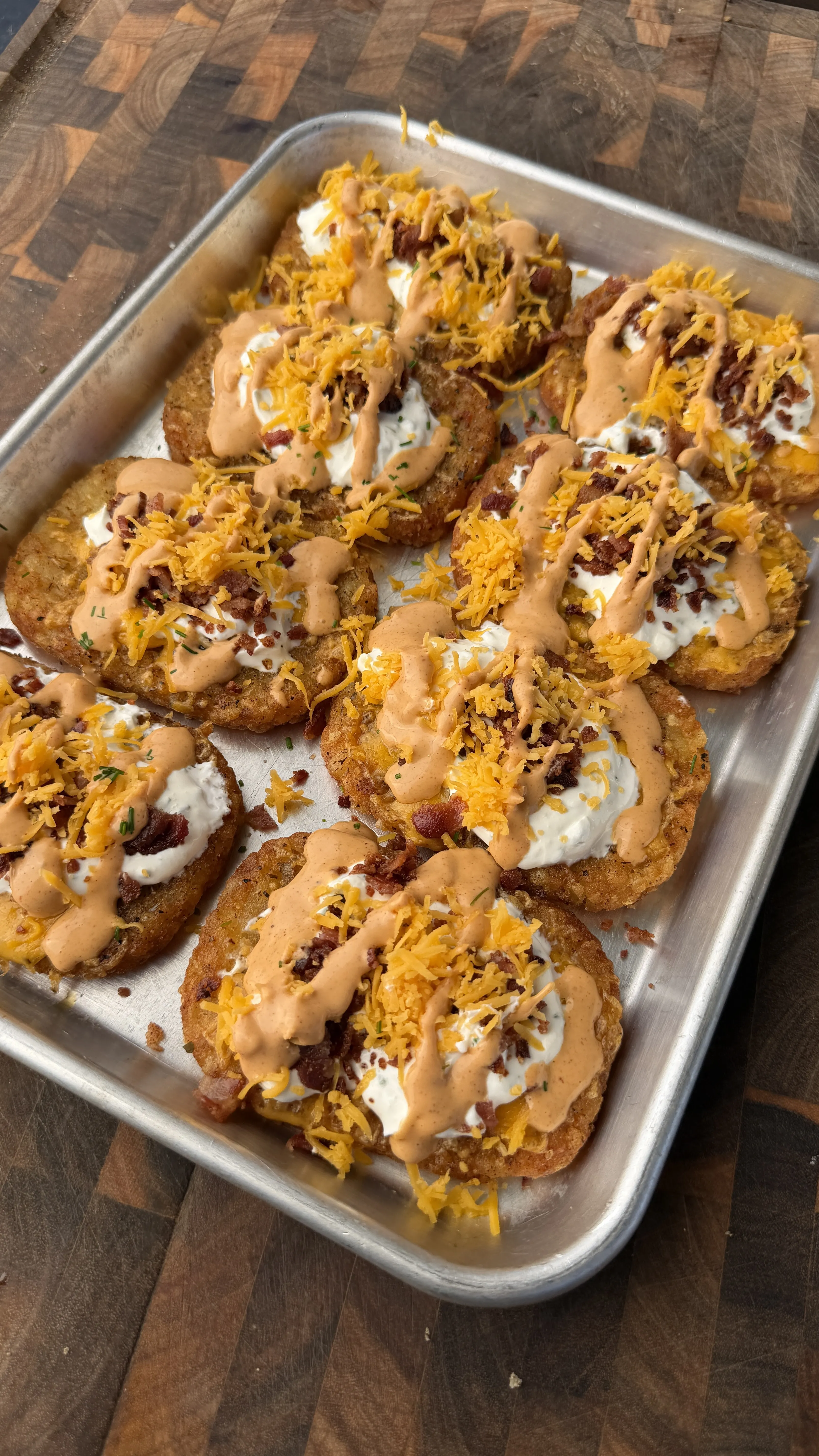 Loaded crispy hash browns topped with sour cream, cheese, bacon bits and sauce on a baking tray