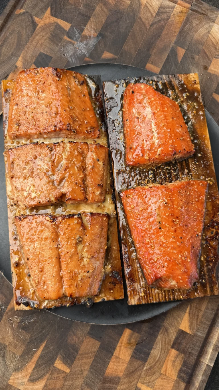 Six glazed maple bourbon salmon fillets on cedar planks with caramelized crust on a dark cutting board
