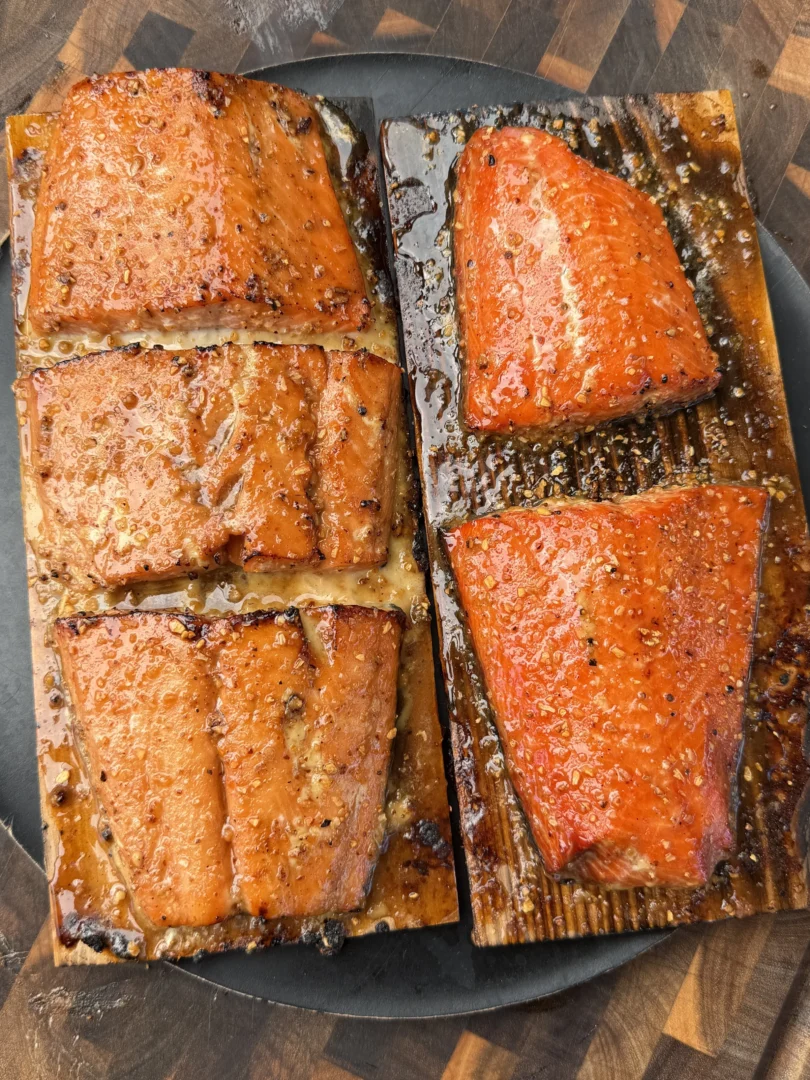 Six glazed maple bourbon salmon fillets on cedar planks with caramelized crust on a dark cutting board