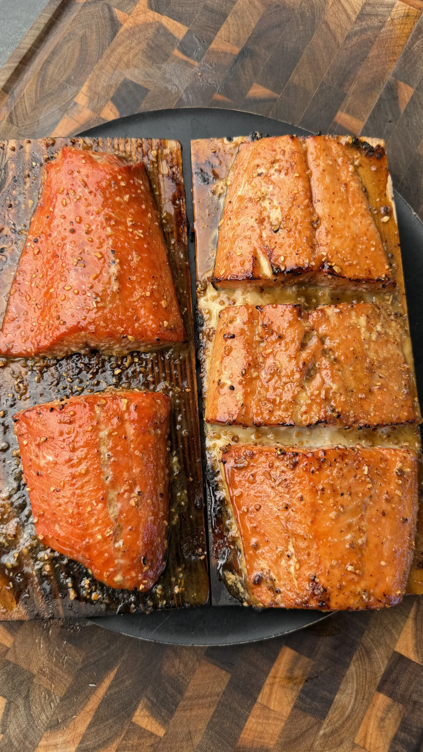Glazed maple bourbon salmon fillets on cedar planks with caramelized crust, served on a dark round plate
