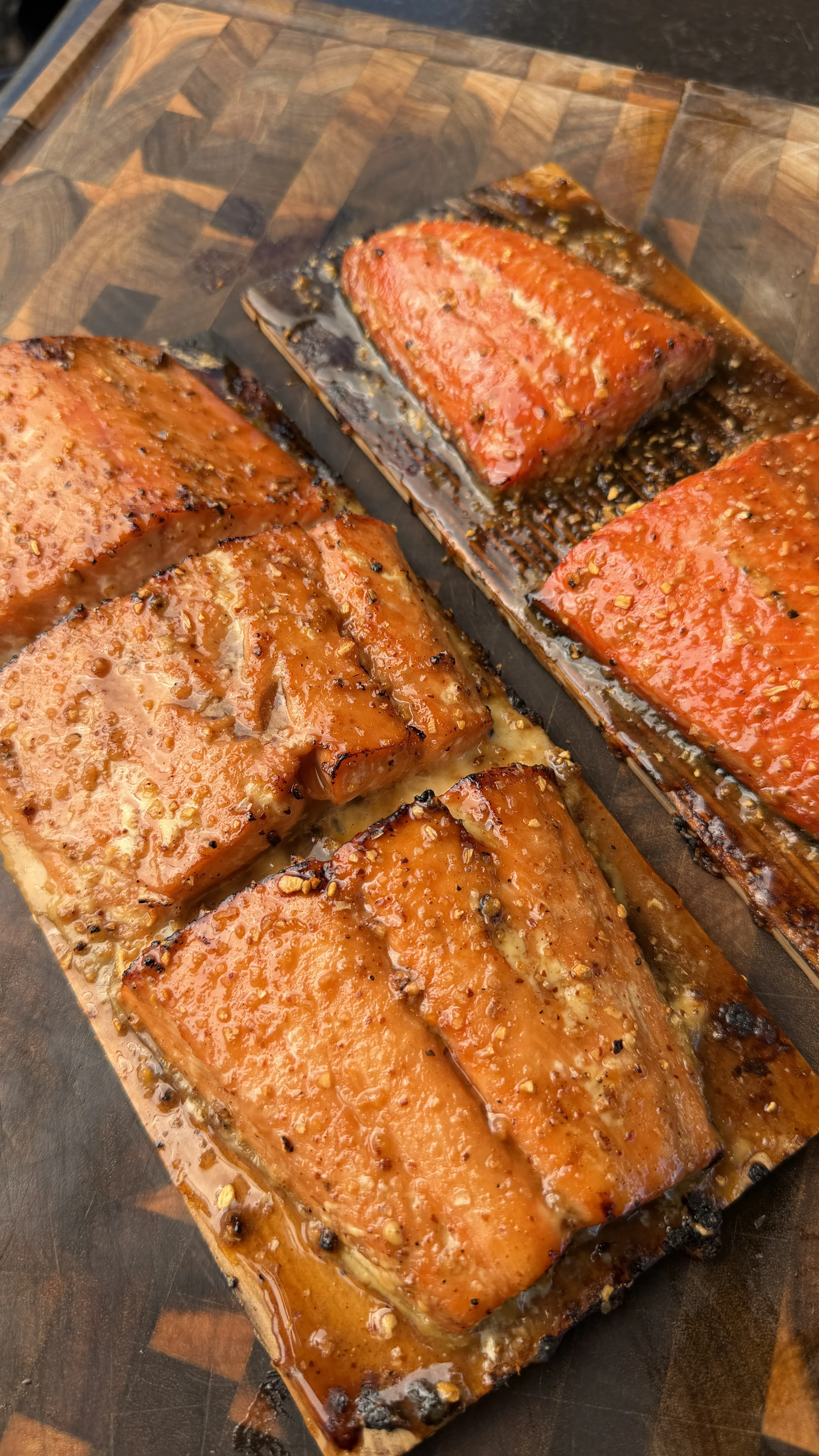 Glazed maple bourbon smoked salmon fillets on cedar planks, resting on a wooden cutting board
