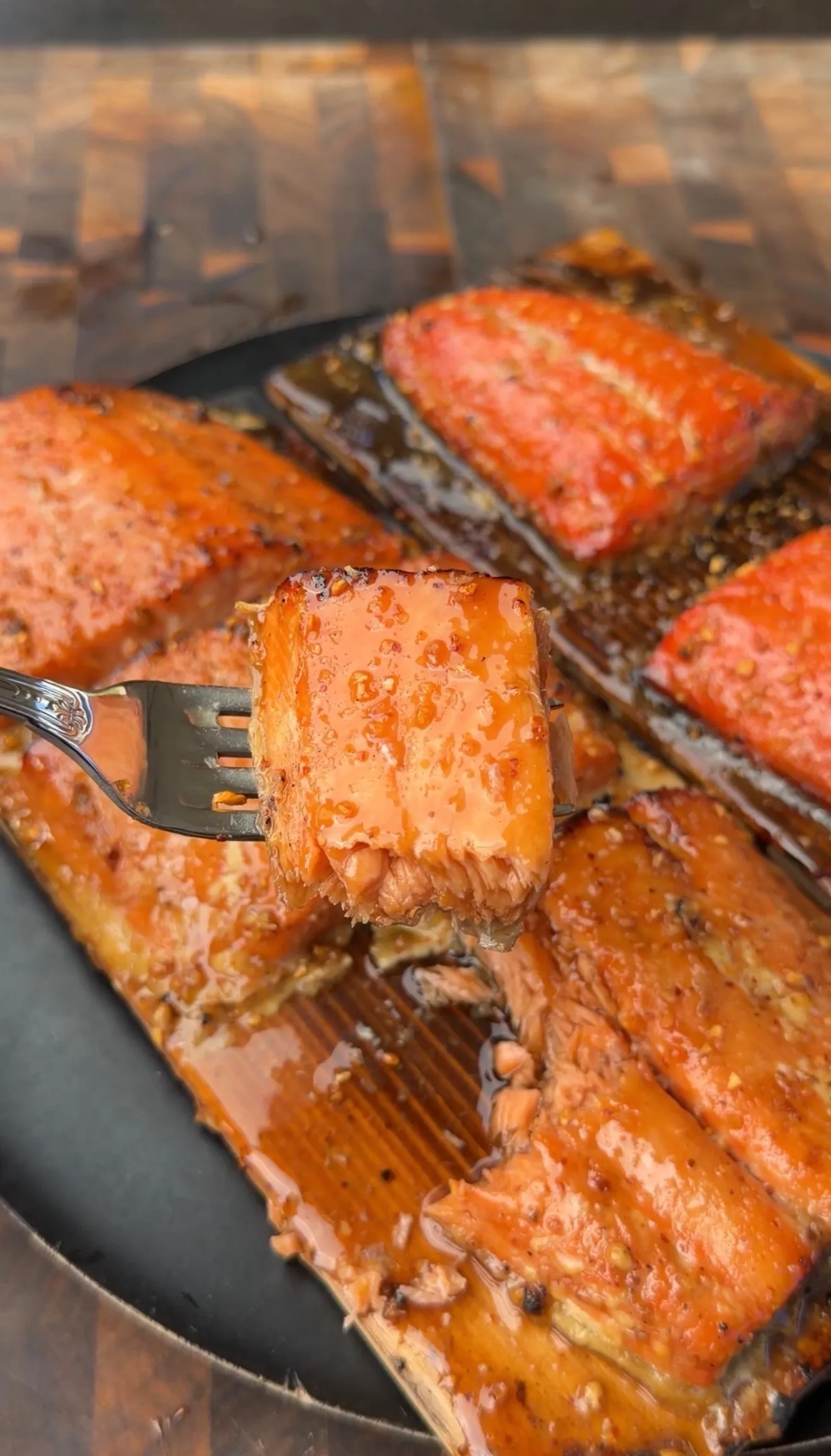 Glazed maple bourbon cedar plank smoked salmon fillets with a fork lifting a caramelized bite