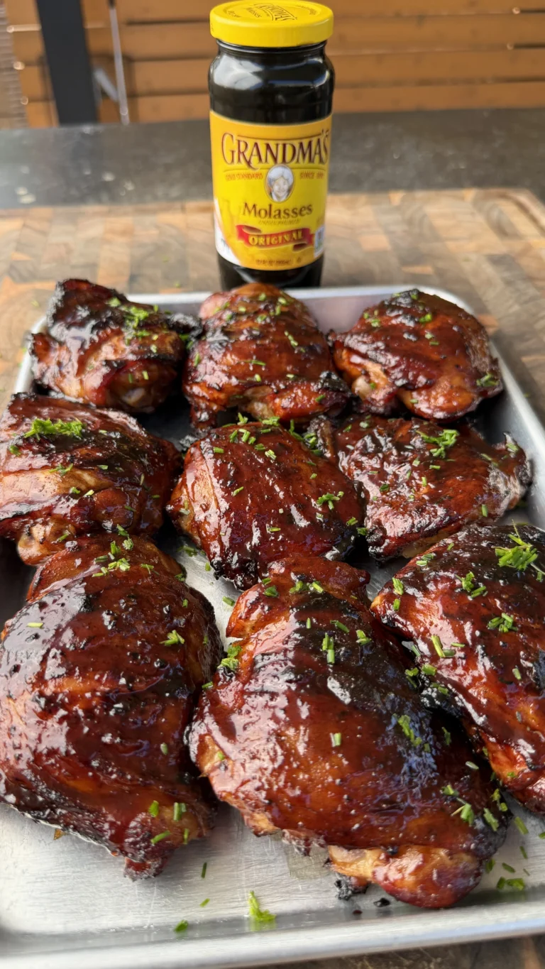 Glazed molasses peach BBQ chicken thighs on white tray with fresh herbs and Grandma's molasses jar