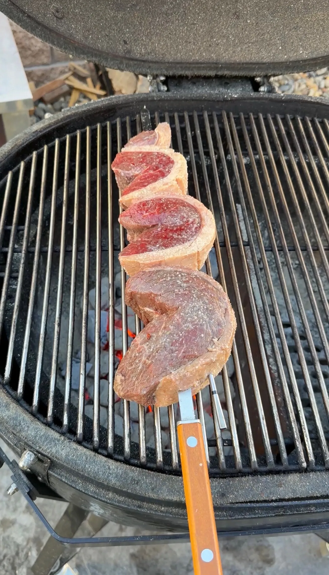 Thick picanha steaks skewered on metal rod cooking over charcoal on round barbecue grill