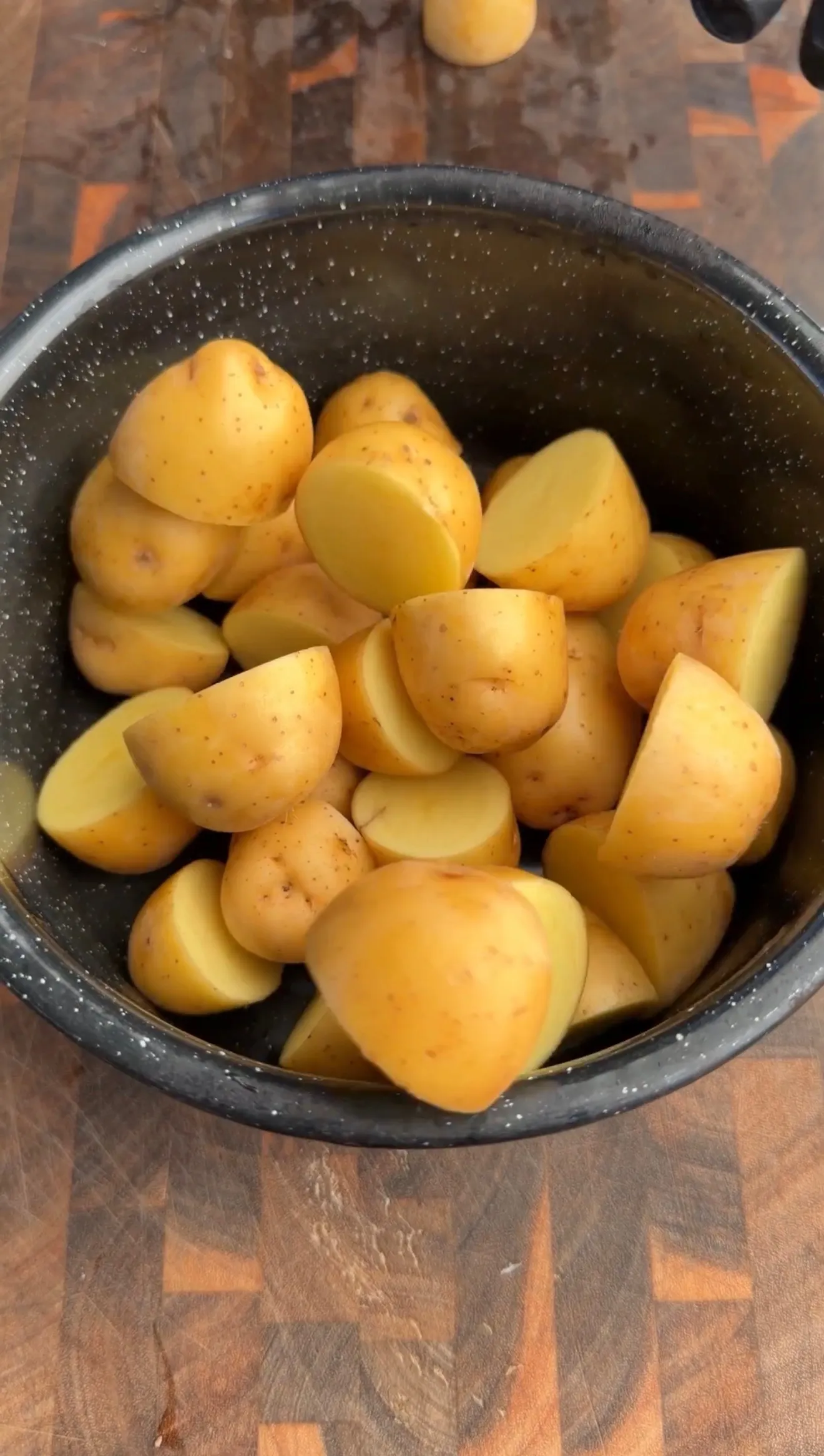 Quartered yellow potatoes in a dark speckled pan, prepped for making crispy Parmesan potatoes