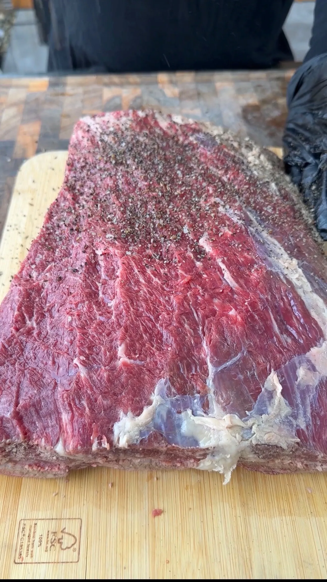 Raw beef plate ribs generously seasoned with salt and pepper rub on a wooden cutting board