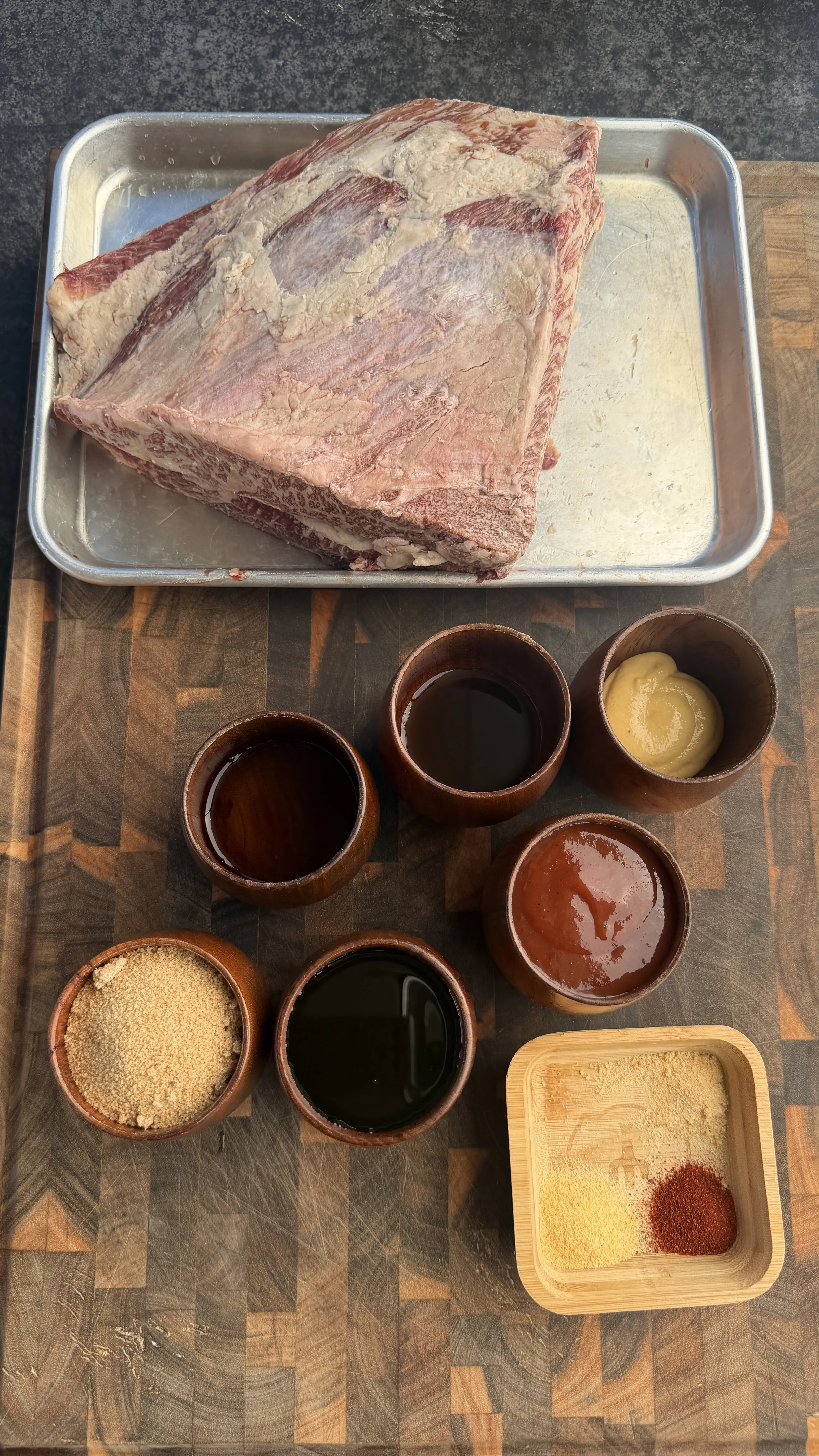 Raw beef ribs on metal tray with bowls of spices, sauces and rub ingredients for smoked burnt ends preparation