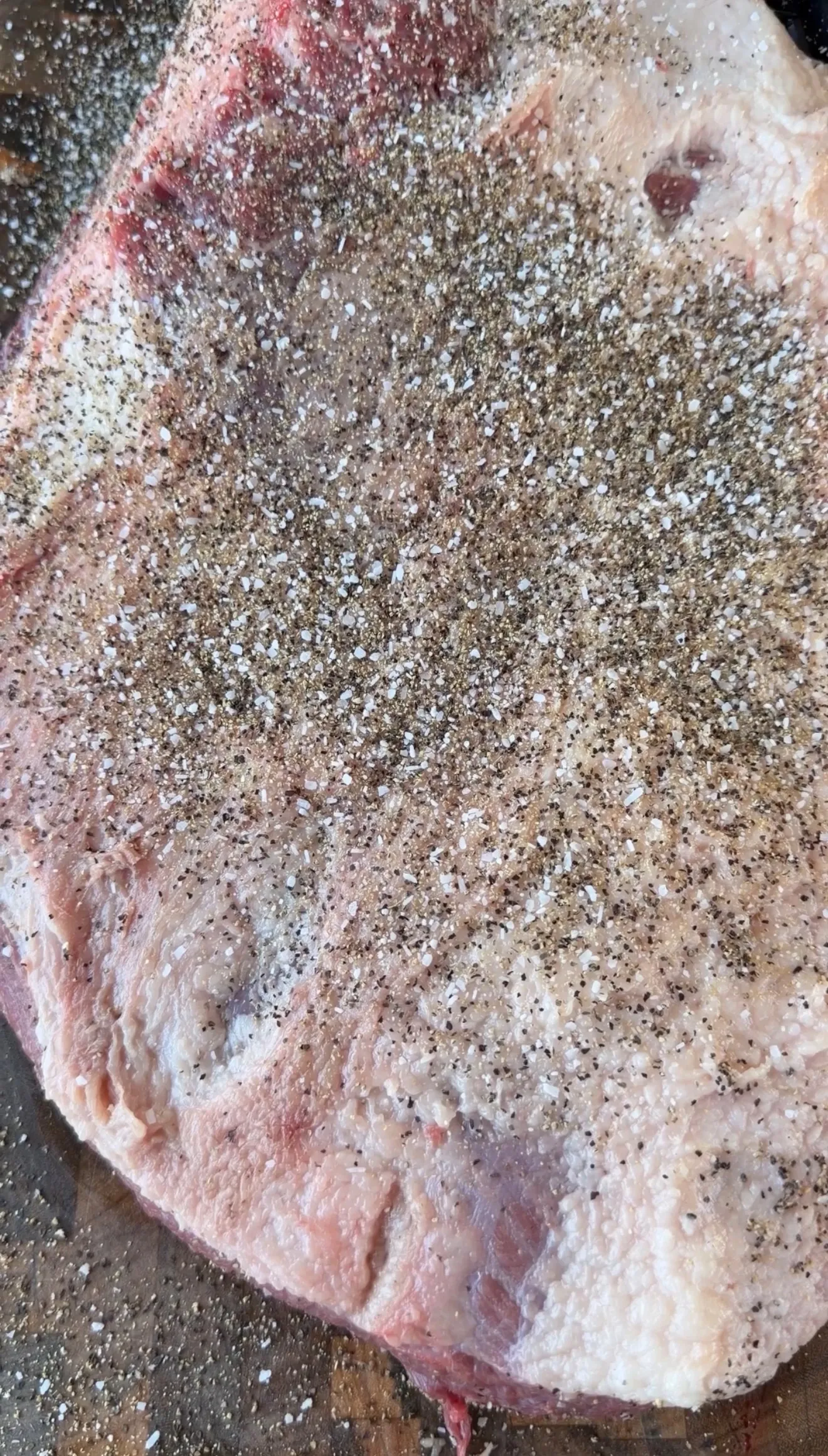 Raw beef brisket generously coated with coarse salt and cracked black pepper before cherry smoking