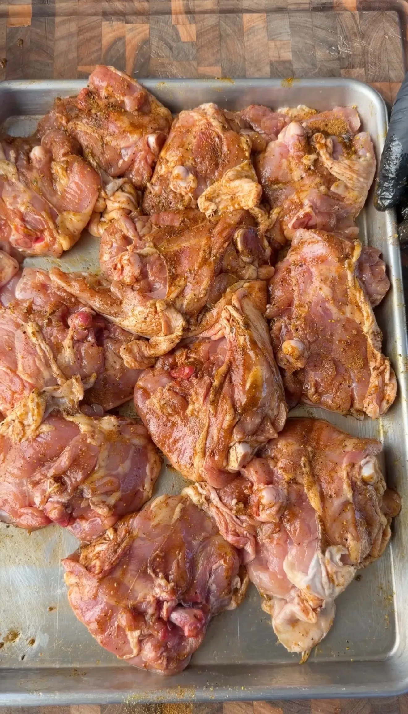 Raw bone-in chicken thighs seasoned with Cajun lemon pepper spice rub on a metal sheet pan