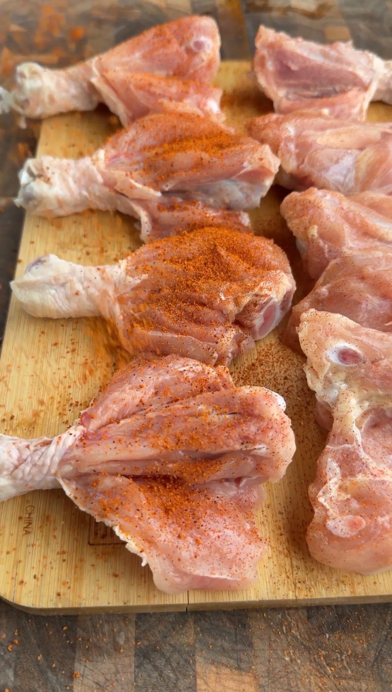 Raw chicken drumsticks seasoned with chili lime spice rub on a wooden cutting board, ready for grilling