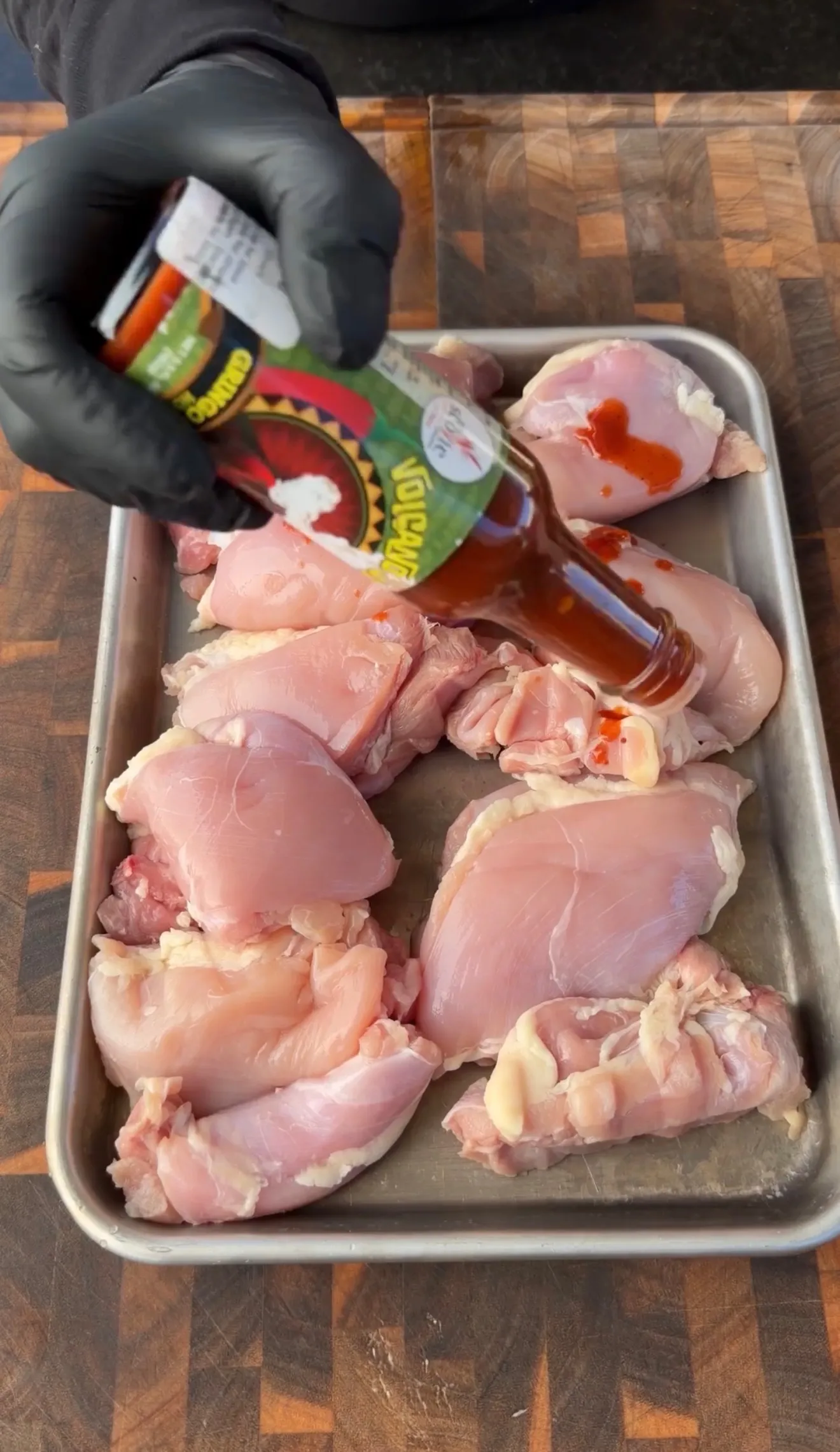 Raw chicken thighs on a sheet pan being seasoned with hot sauce for a spicy chicken BLT sandwich