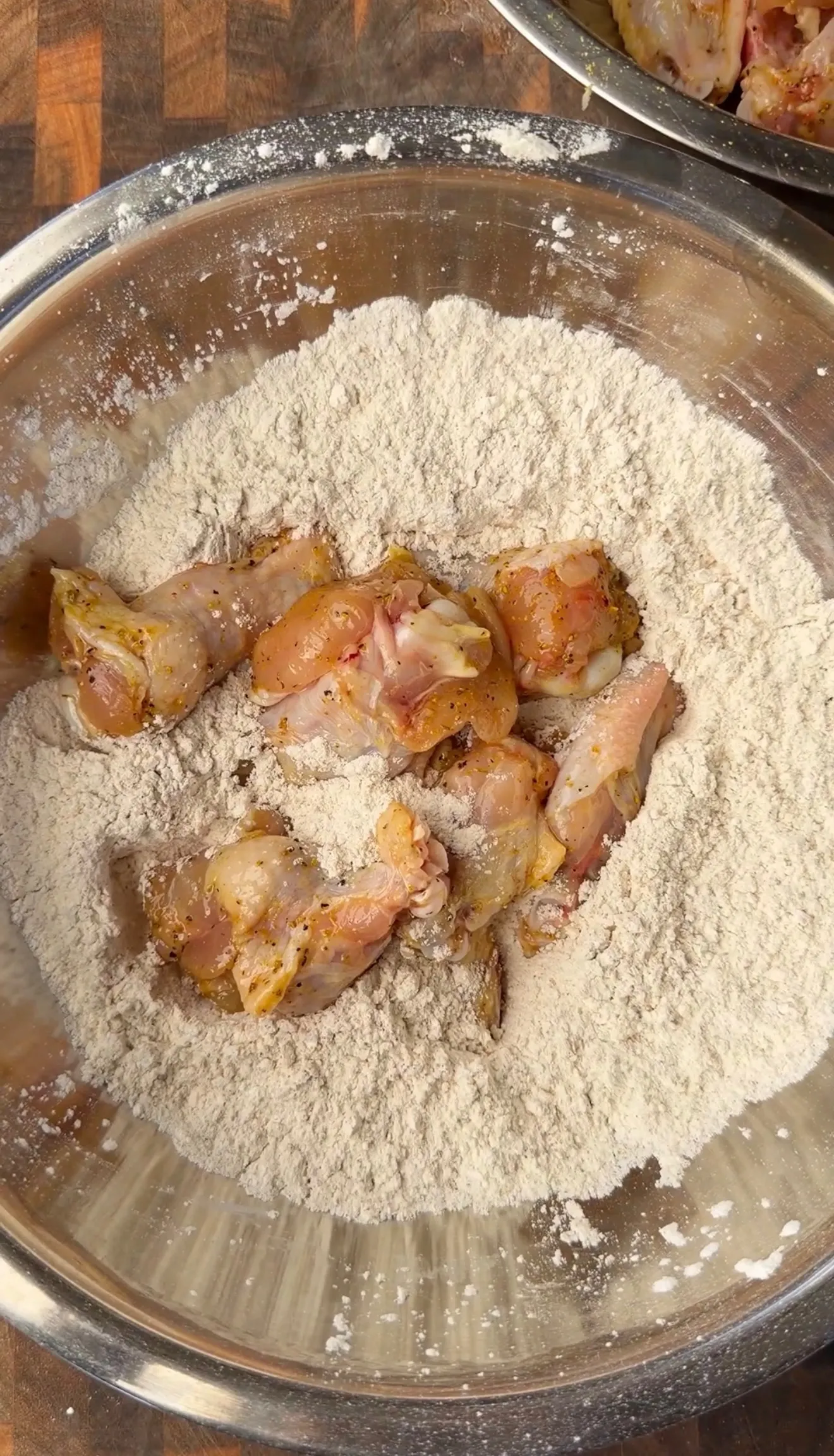 Raw honey lemon pepper chicken wings being dredged in seasoned flour inside a large stainless steel mixing bowl