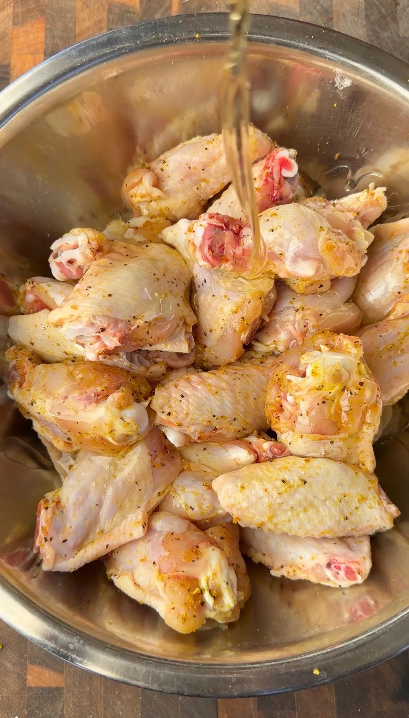Raw chicken wings seasoned with lemon pepper spices in a stainless steel mixing bowl