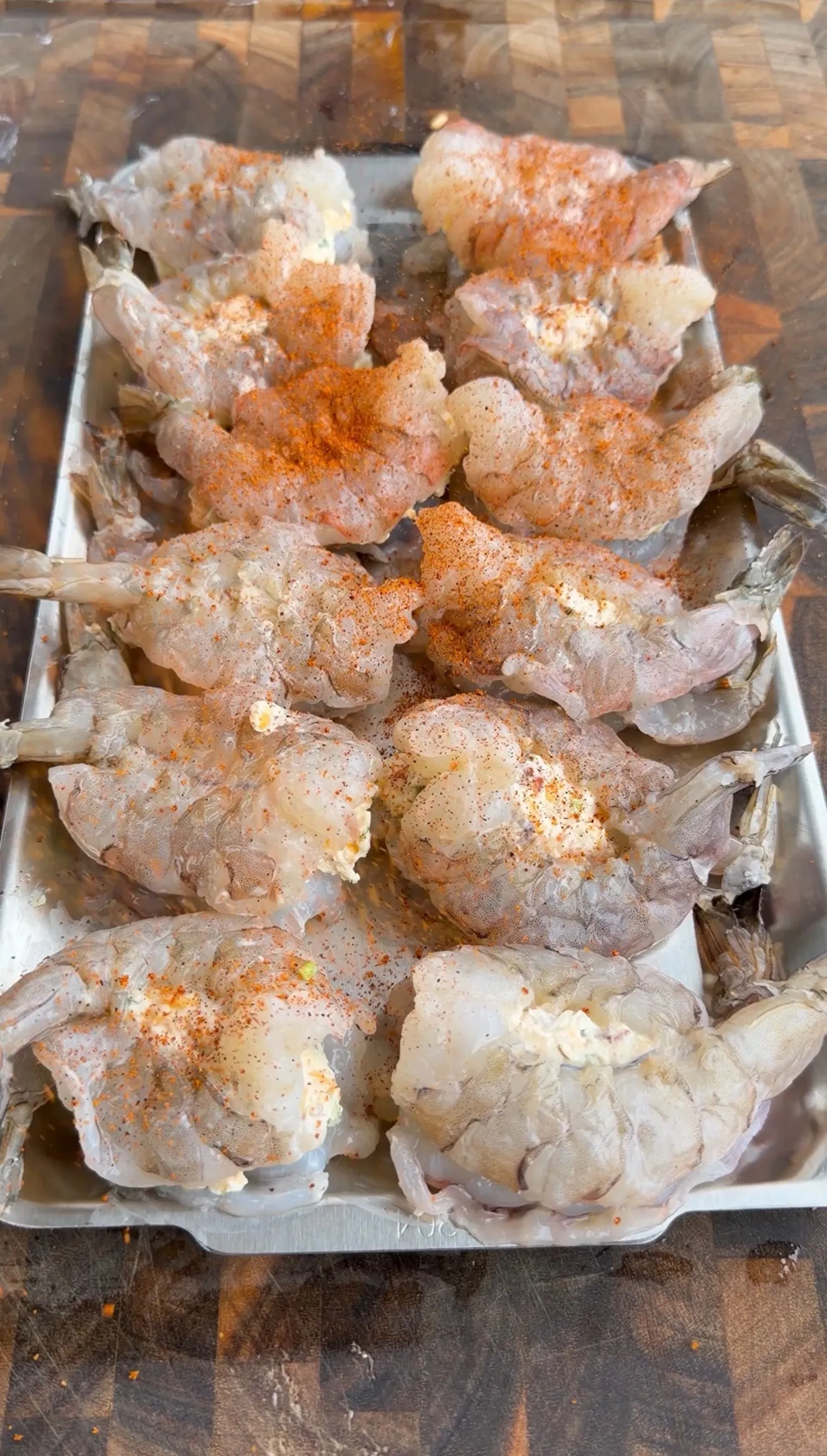 Raw jumbo shrimp stuffed with jalapeño popper filling arranged on a metal tray
