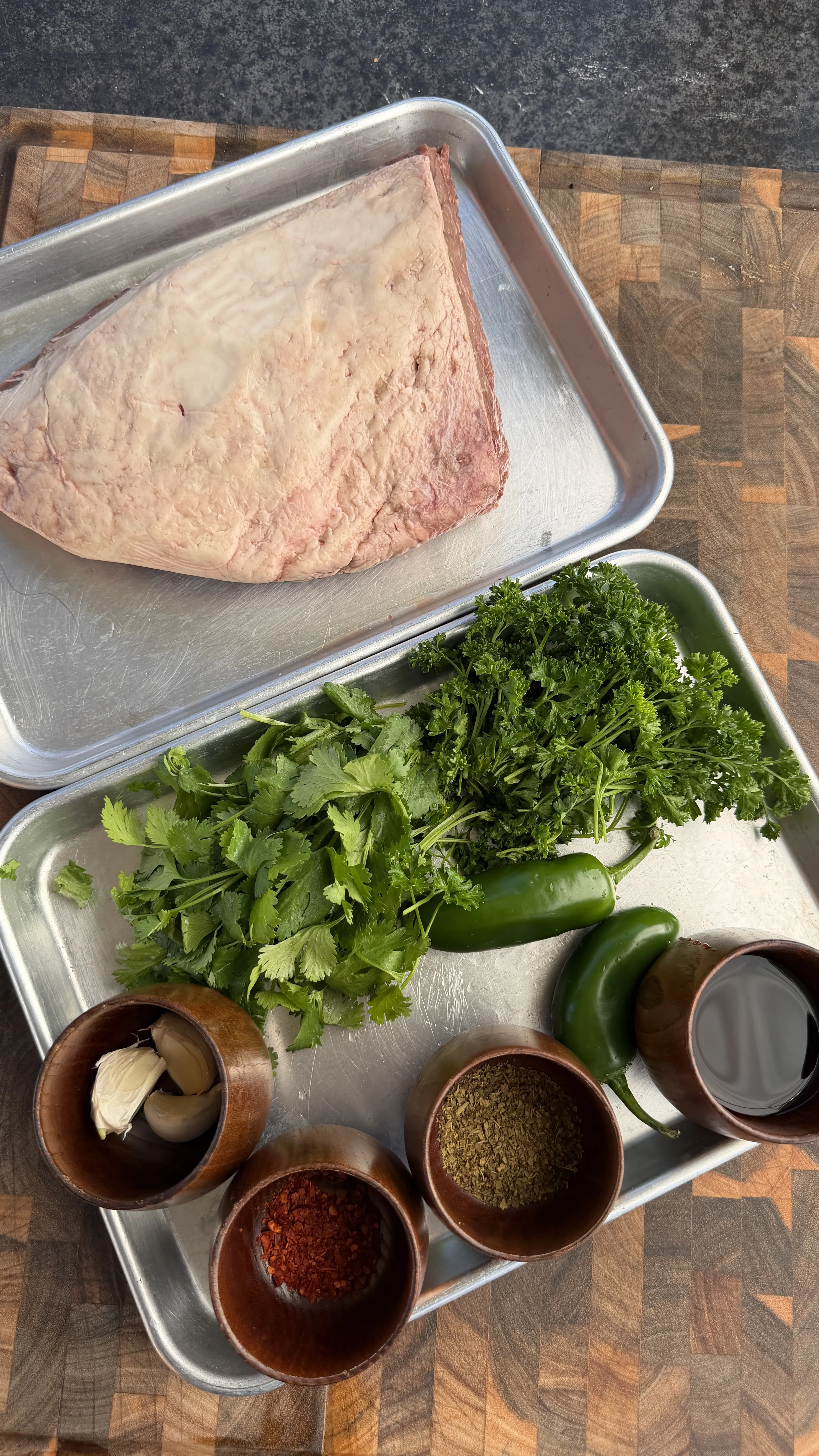 Raw picanha steak on metal tray with fresh cilantro, jalapeños, garlic and spices for chimichurri preparation