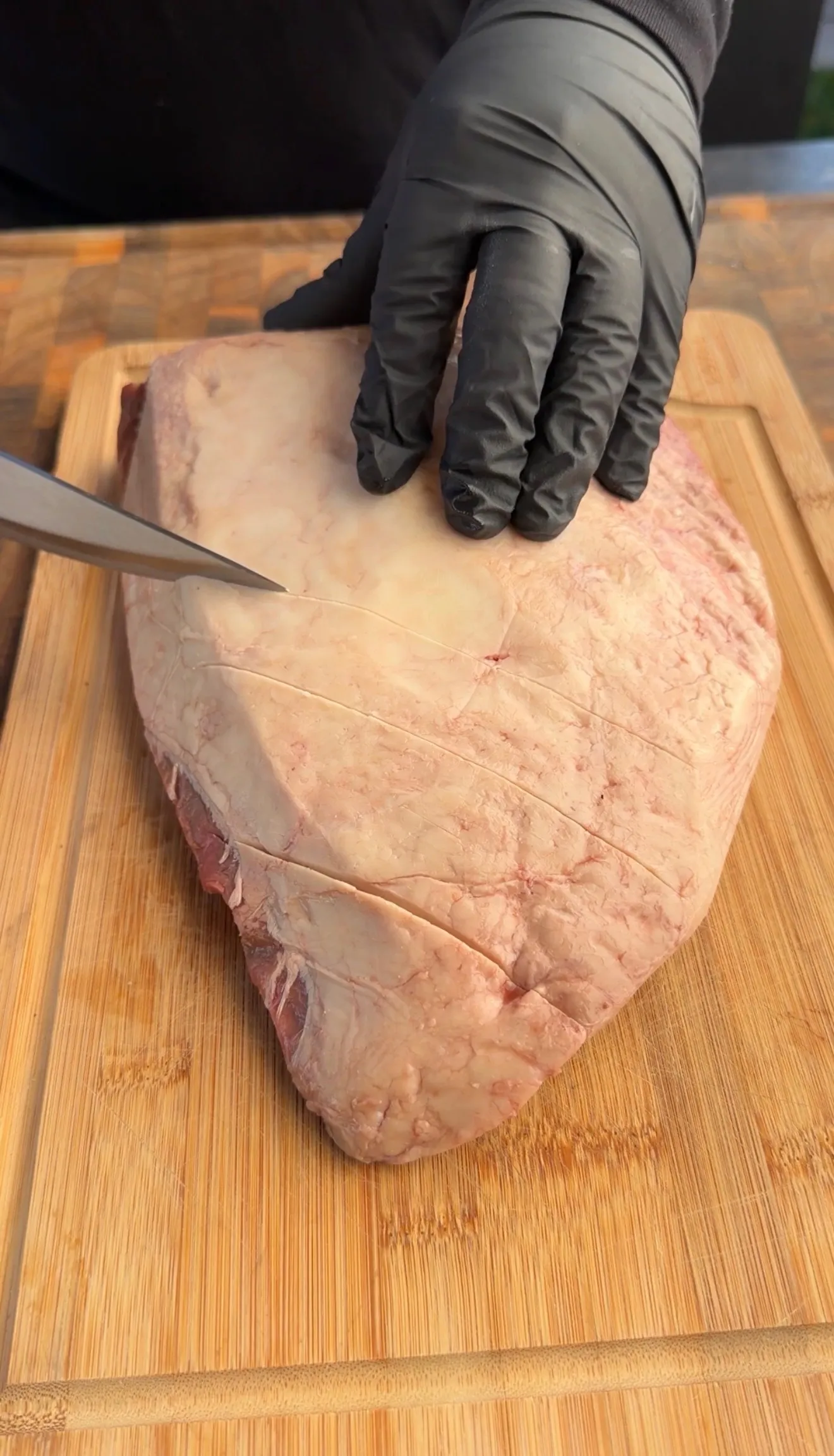 Raw picanha steak with crosshatch scoring marks being prepared on wooden cutting board with knife and gloved hands