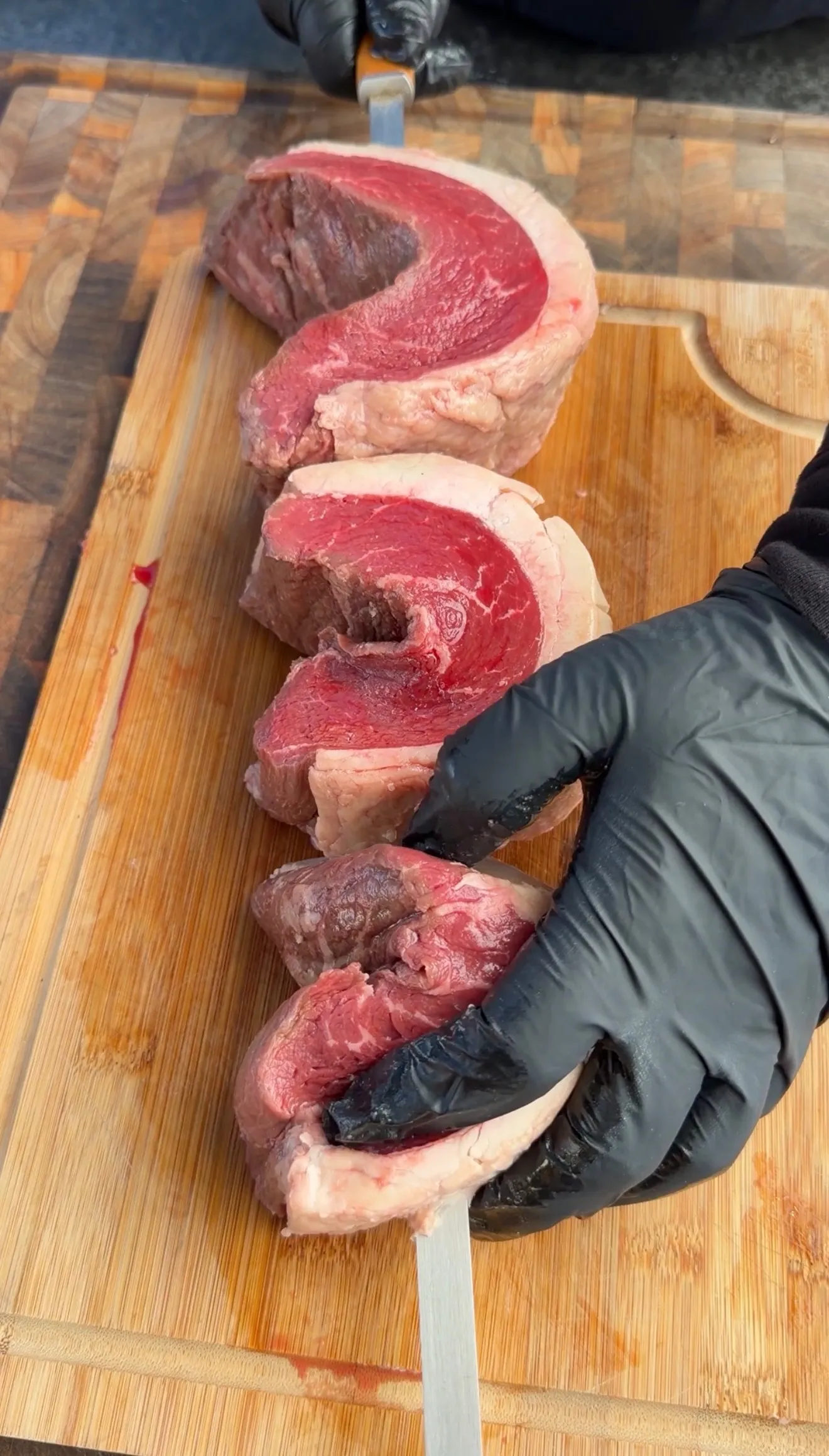 Raw picanha beef steaks sliced on wooden cutting board showing marbled red meat with fat cap