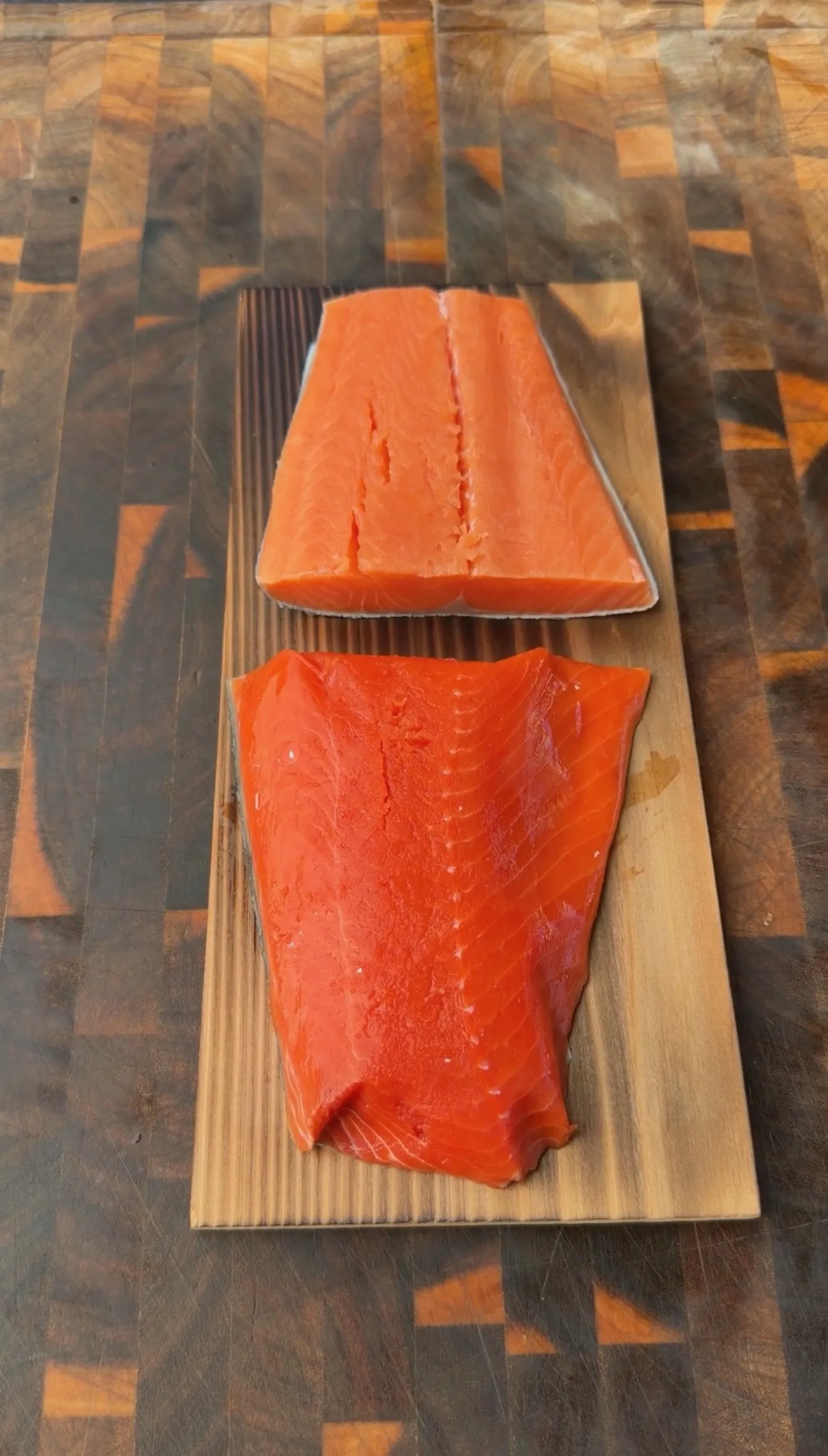 Two fresh raw salmon fillets on a cedar plank over a rustic wood cutting board, ready for smoking