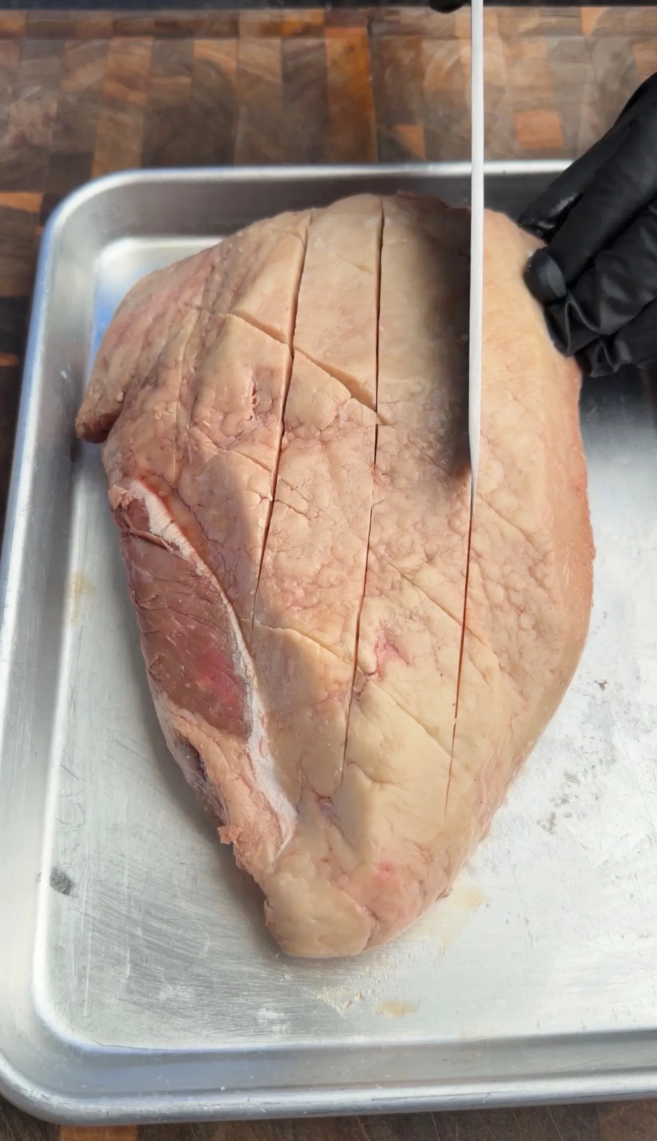 Raw picanha roast with diagonal score marks on aluminum cutting board, ready for smoking preparation