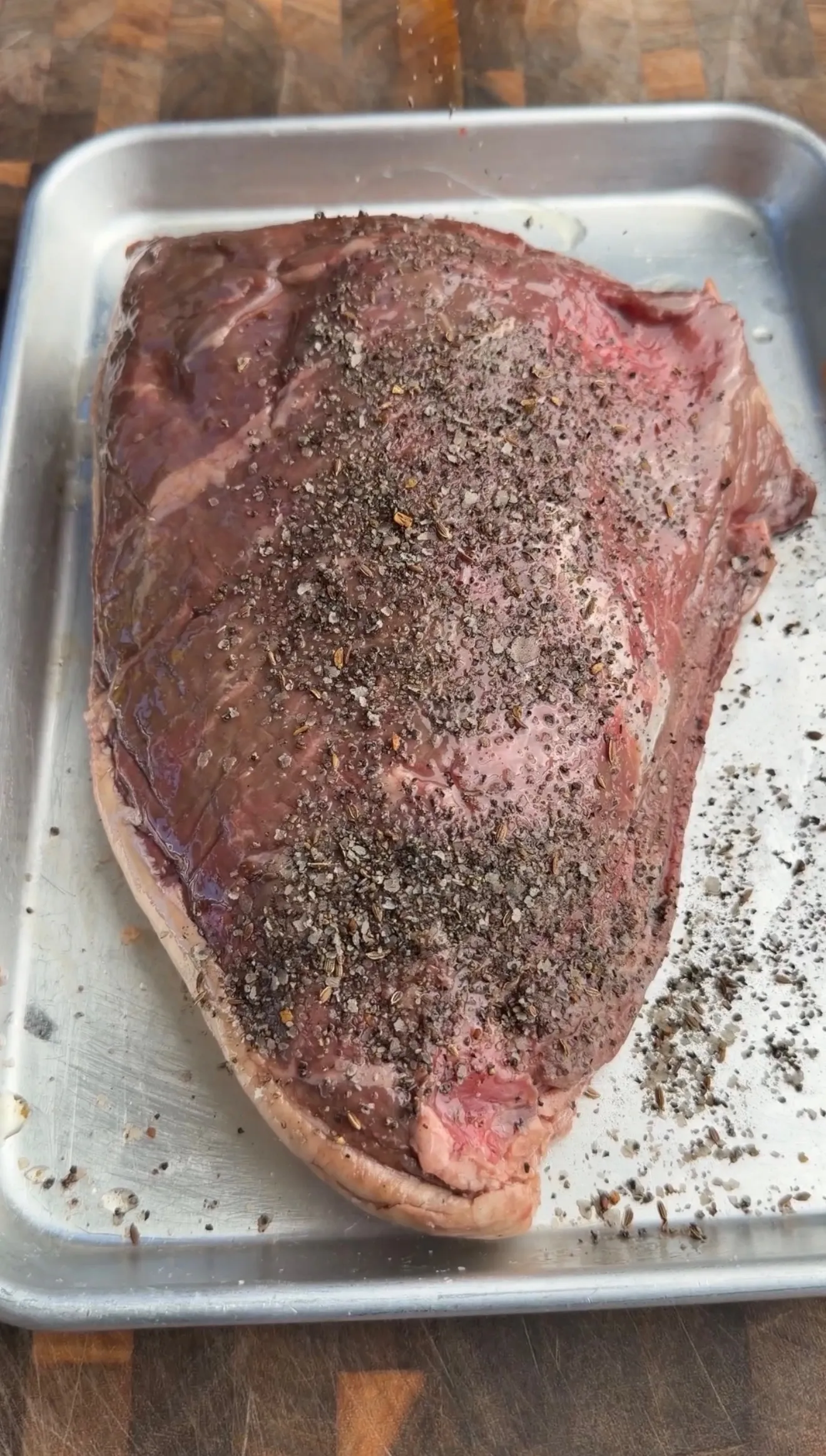 Raw picanha roast seasoned with black pepper and spices in metal baking pan, ready for smoking