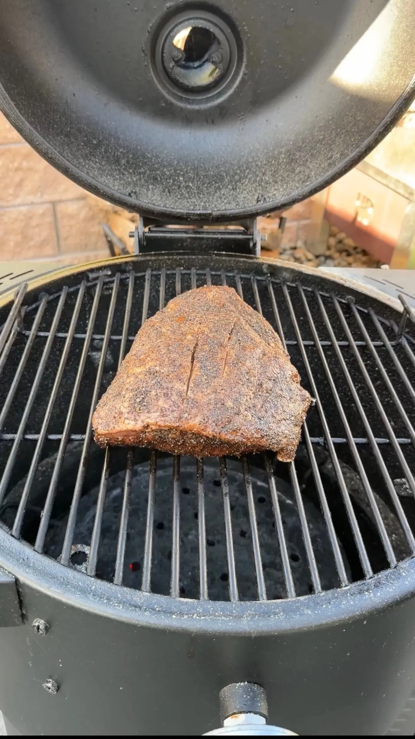 Seasoned picanha roast with spice rub cooking on grill grates inside an open kamado-style smoker