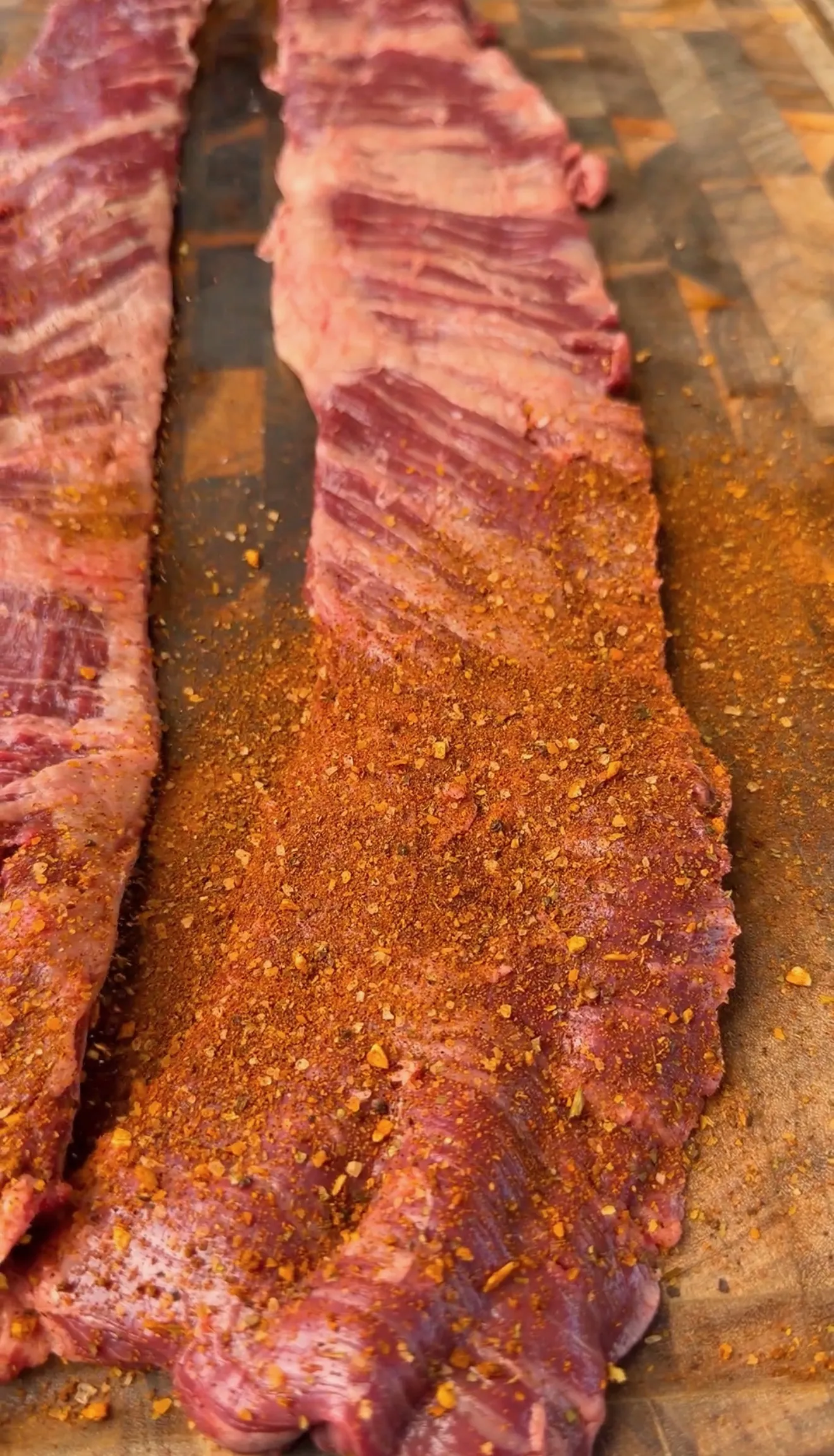 Raw skirt steak seasoned with spice rub on wooden cutting board, ready for cooking tacos