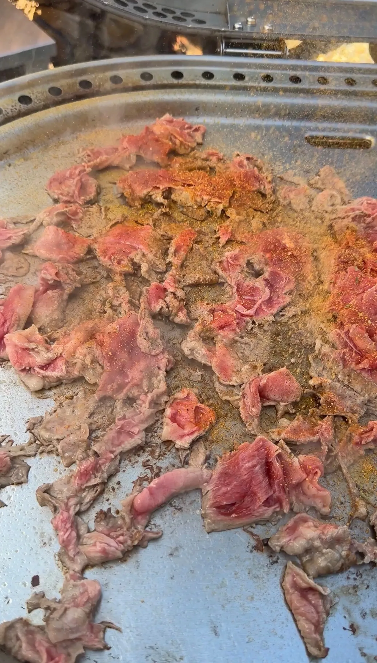 Thin-sliced seasoned beef with spices cooking on a flat iron griddle for cheesesteak stuffed bolillo bread