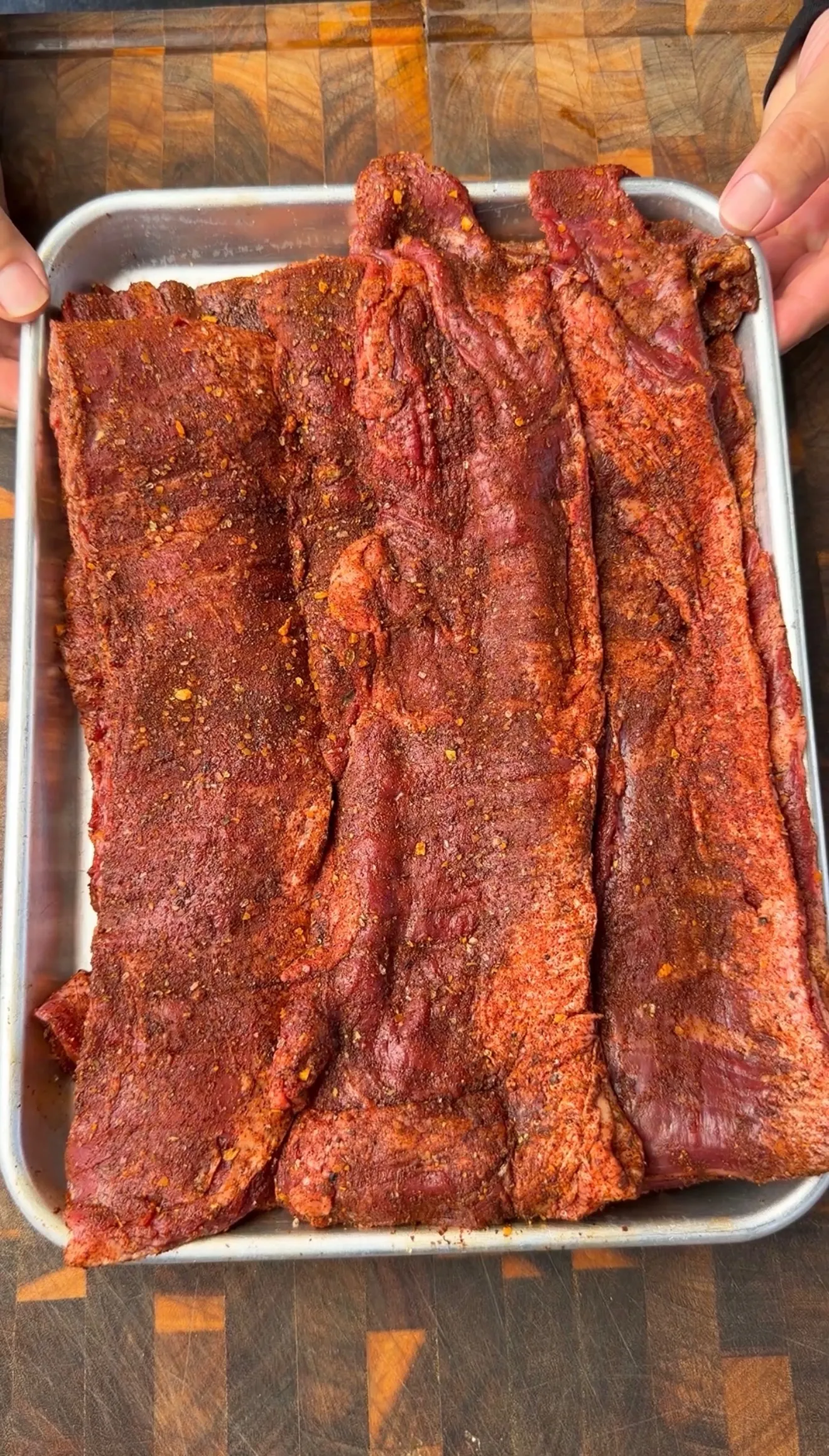 Raw skirt steak coated with red chipotle spice rub on aluminum tray, ready for cooking