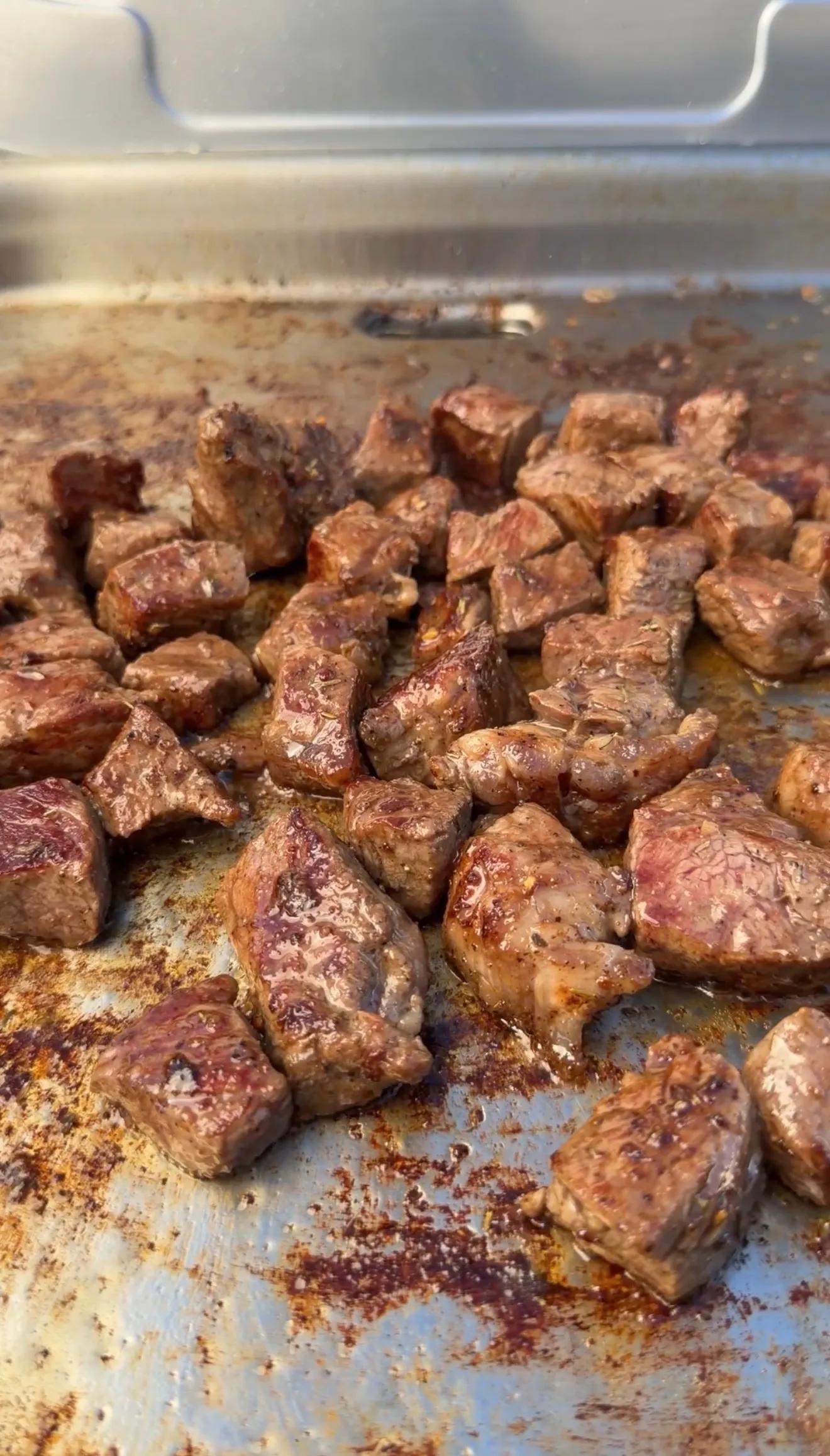 Juicy seasoned steak bites seared golden brown on a flat top griddle for smashed steak loaded potatoes