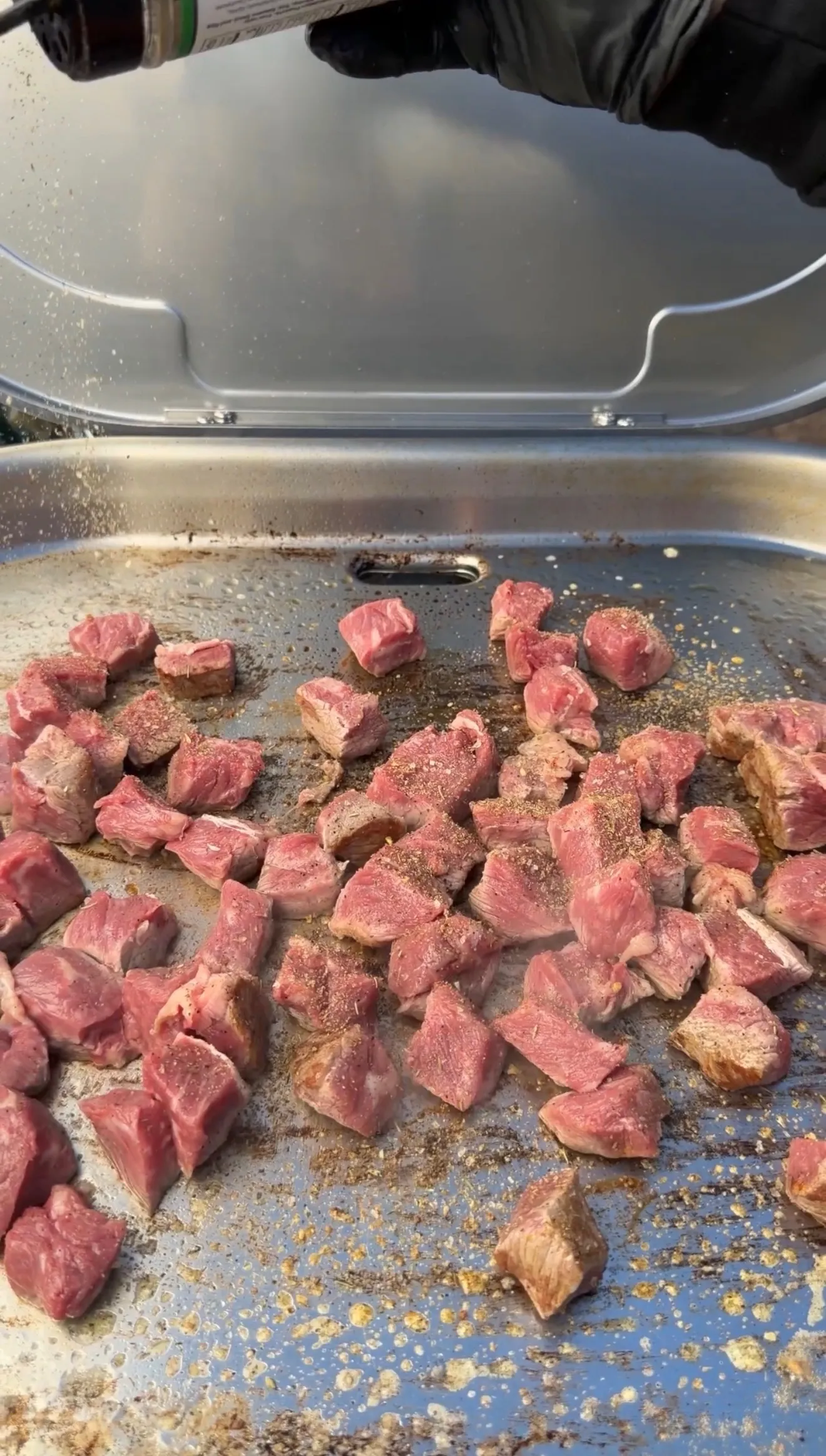 Cubed steak bites seasoned with black pepper searing on a flat top griddle for smashed steak loaded potatoes