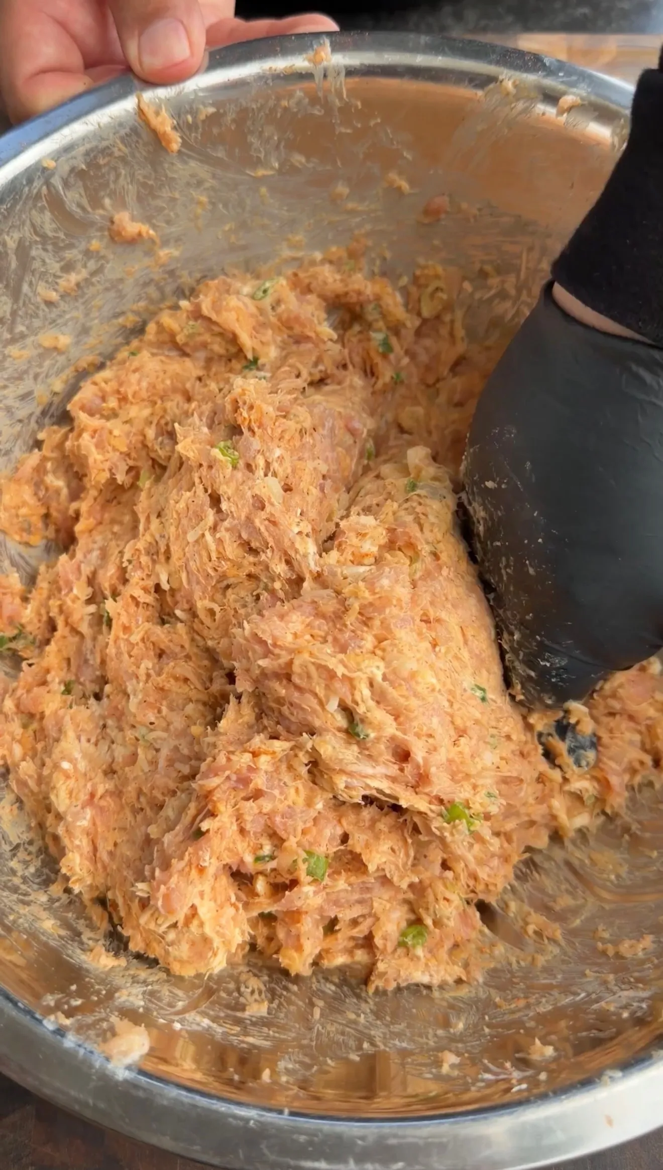 Shredded buffalo chicken mixture with herbs in a clear glass mixing bowl being prepared for tortilla kebabs