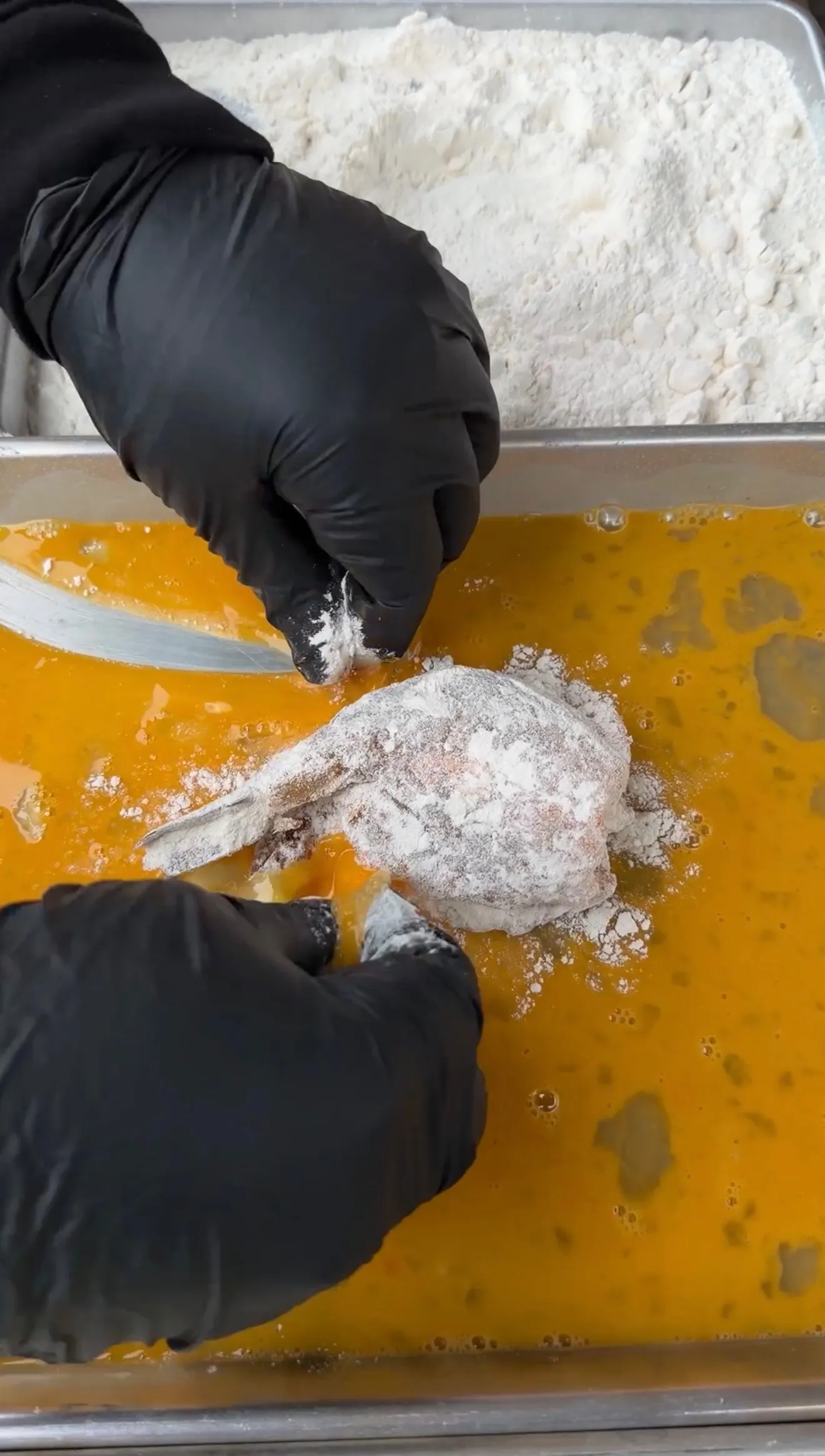 Gloved hands dipping flour-coated stuffed shrimp into beaten egg wash for frying preparation