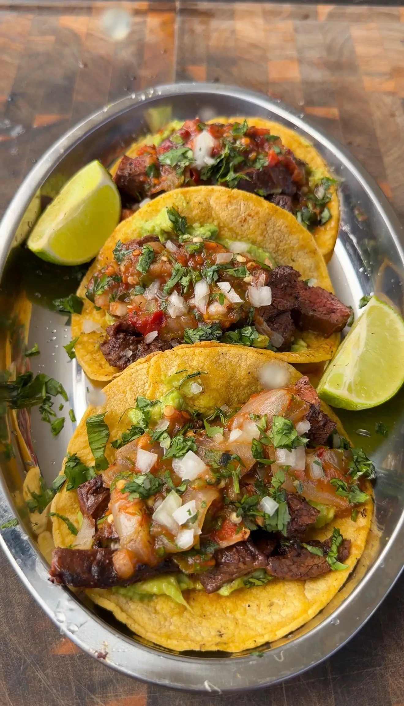 Three skirt steak tacos with chipotle salsa, diced onions, and cilantro on corn tortillas with lime wedges
